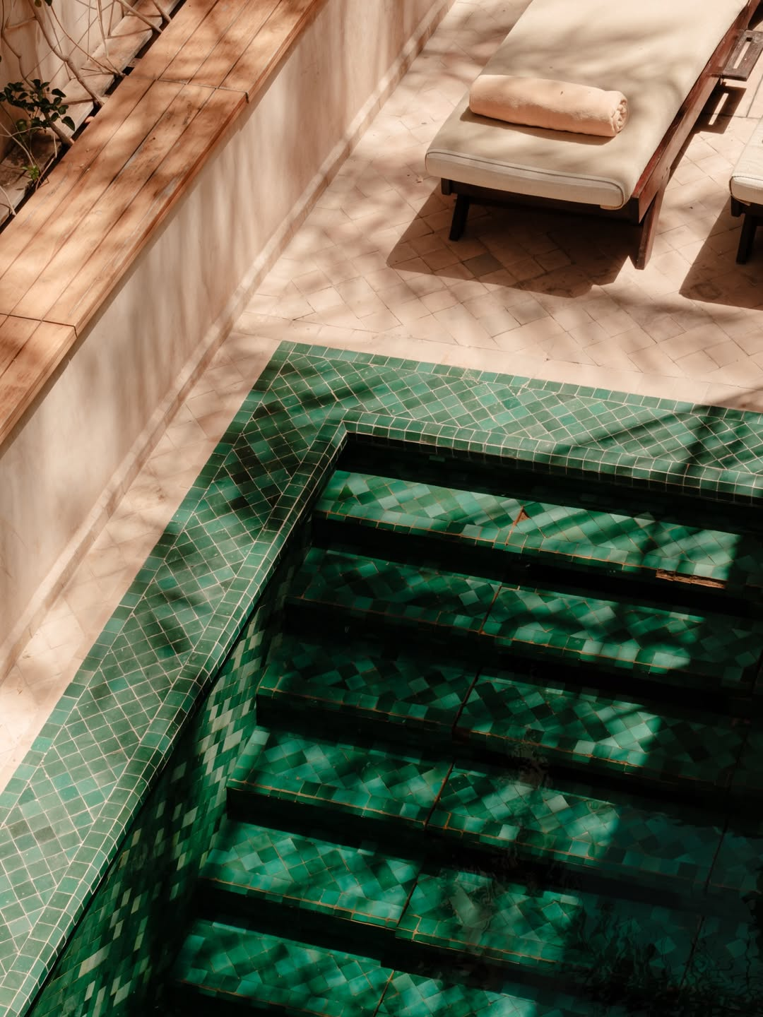 A staircase with green tiled sides leading below an indoor seating area with a lounge chair and blanket, and a wooden ledge with plants.