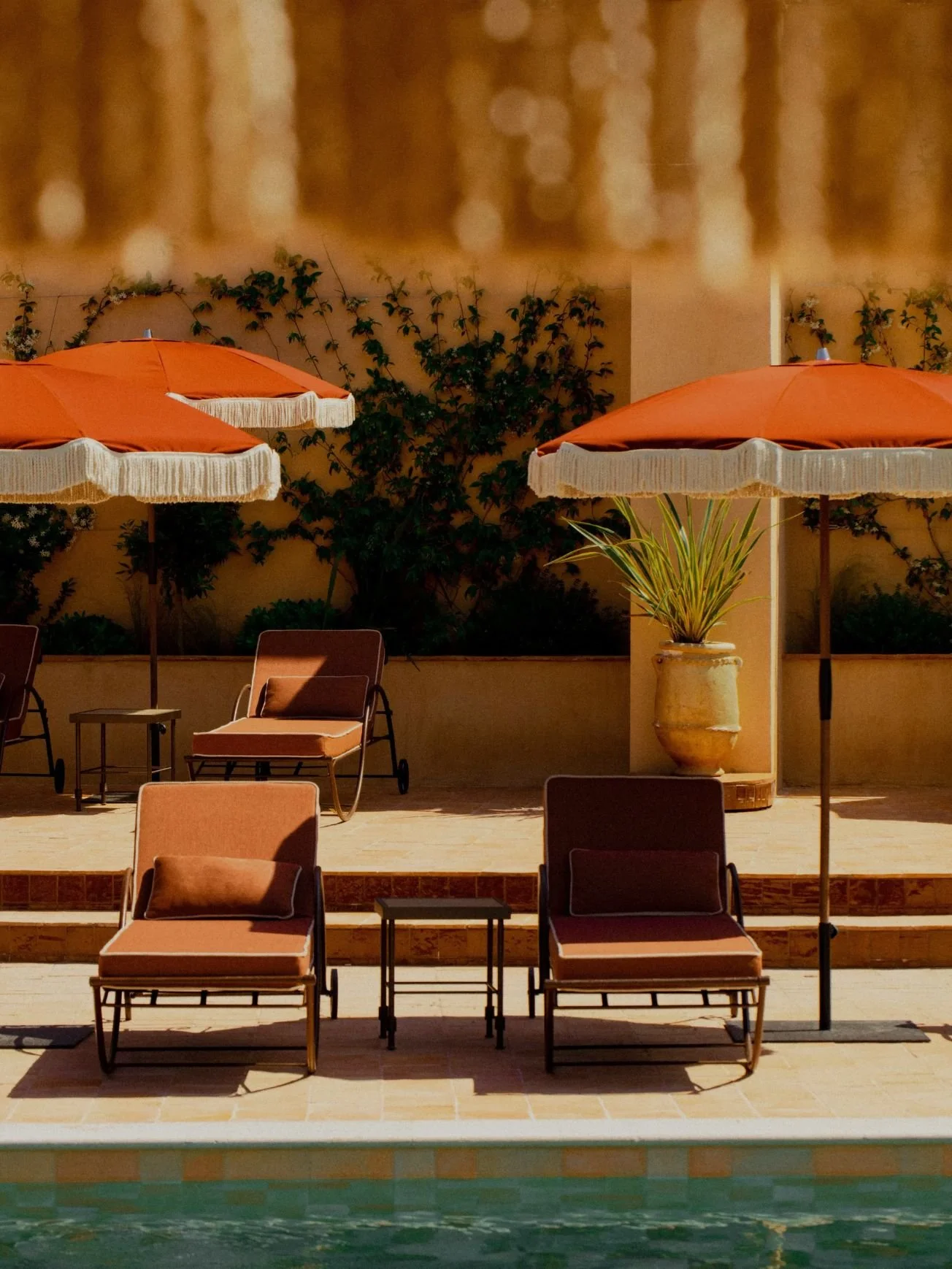 View of a poolside patio with lounge chairs, orange umbrellas, and potted plants.