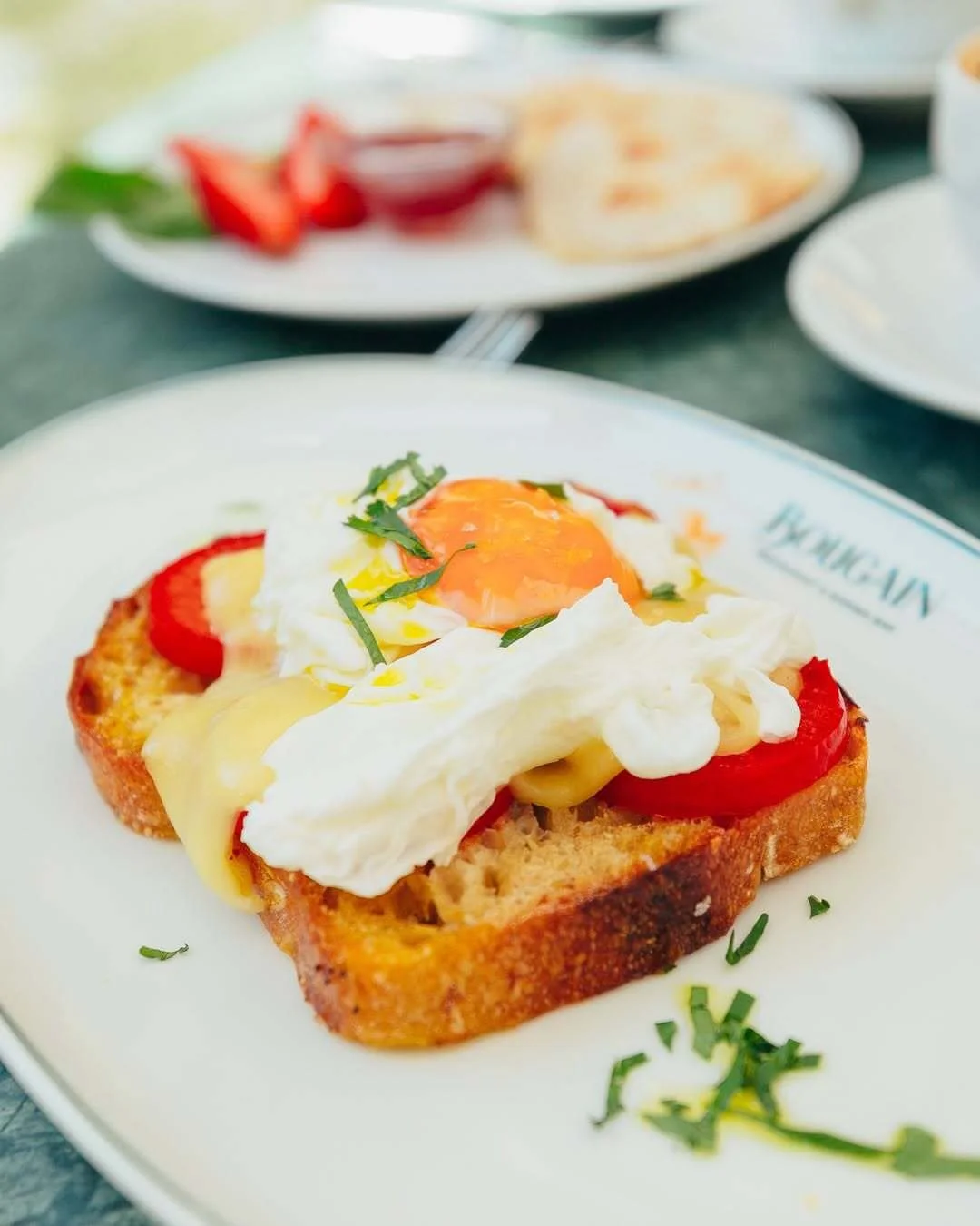 Open-faced breakfast sandwich with an egg, slices of tomato, melted cheese, on toasted bread, garnished with chopped herbs.