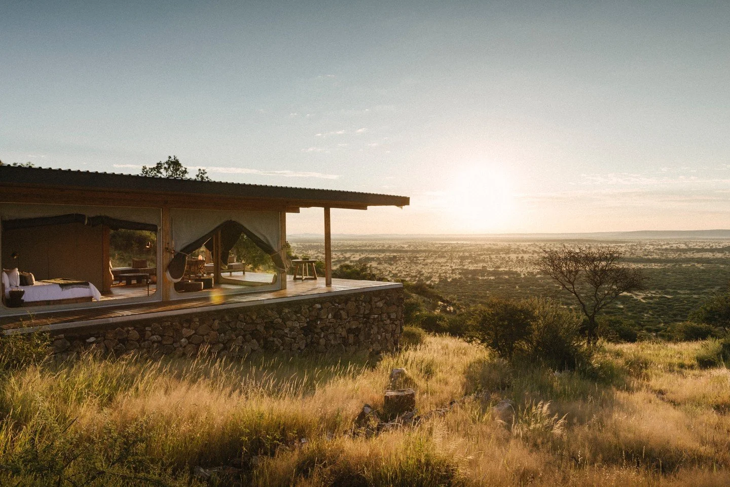 Modern house with large windows overlooking a sunset landscape of open grassland and sparse trees.