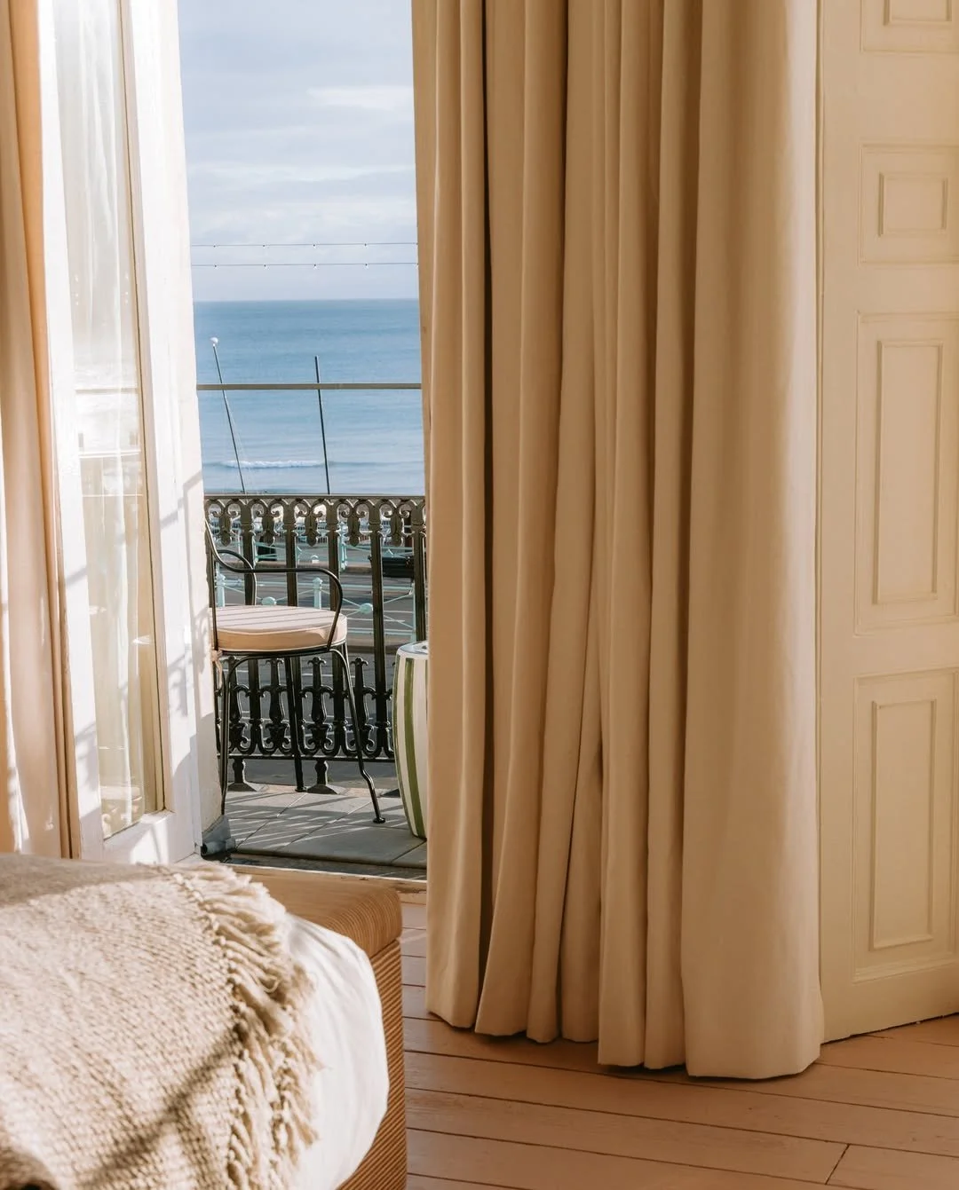 View of a seaside balcony with a chair, partly hidden by a curtain, overlooking the ocean.