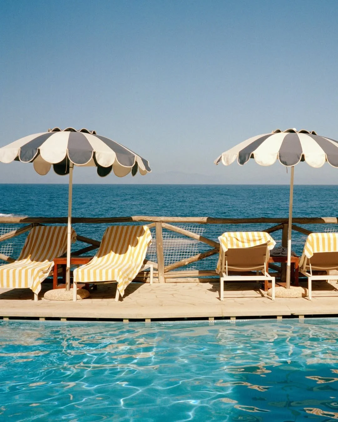 Poolside view with lounge chairs and large umbrellas facing the ocean.