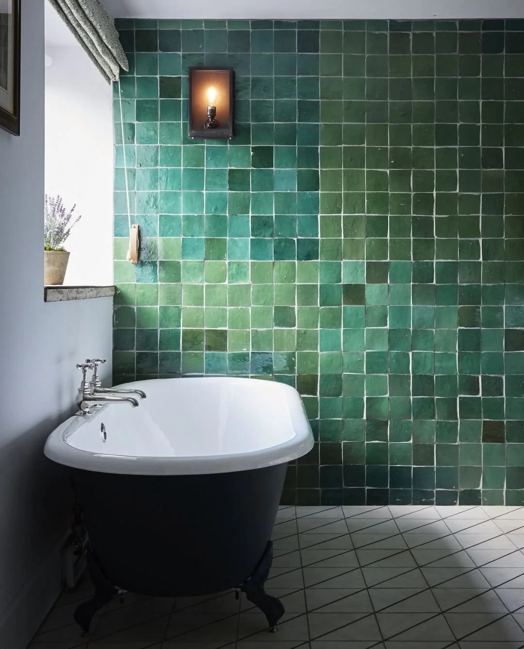 A vintage bathtub with black exterior and white interior in a bathroom with green tiled wall and diamond patterned floor tiles.