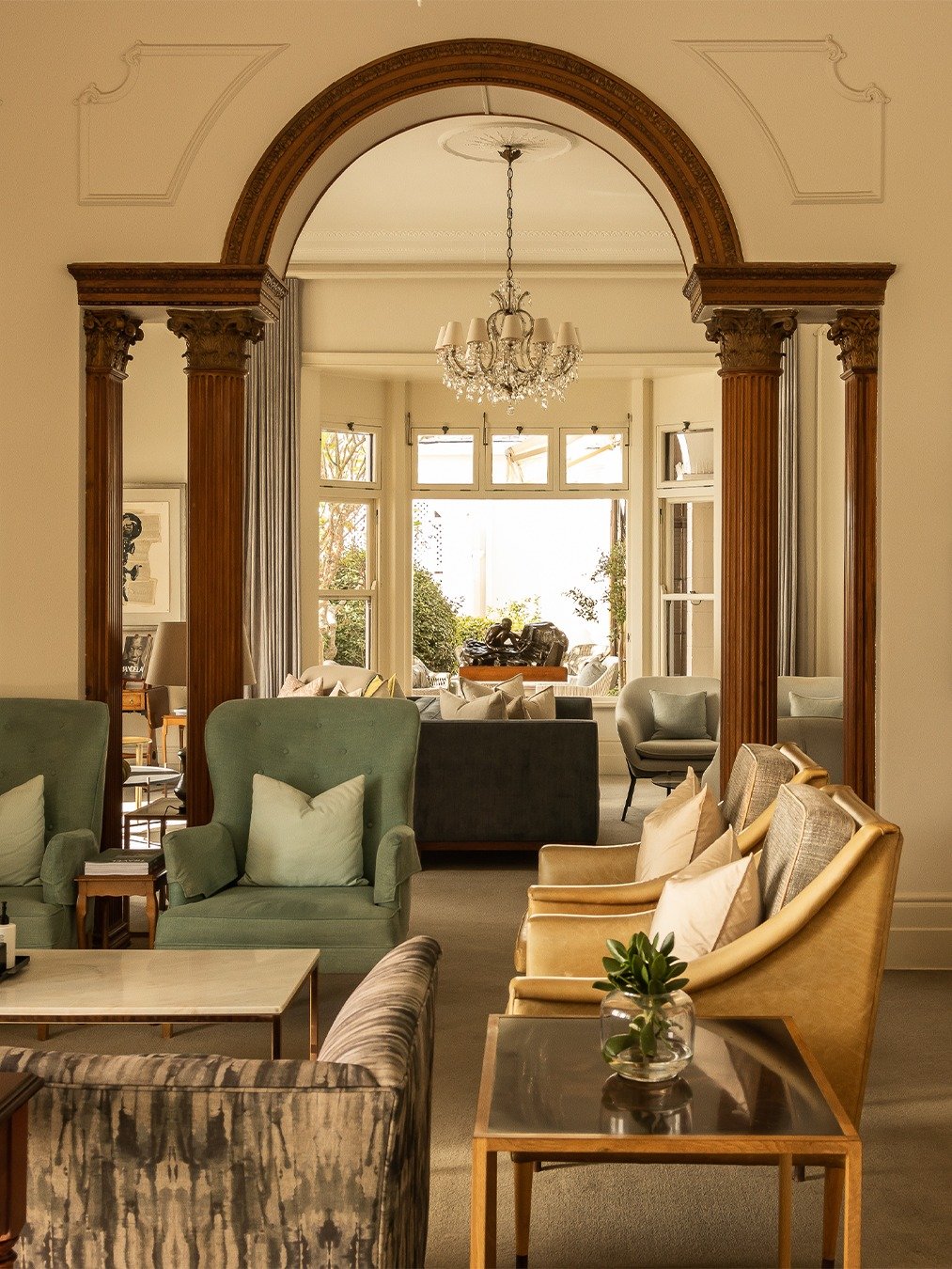 Elegant living room with a decorative archway, large window, chandelier, and assortment of armchairs and sofas.