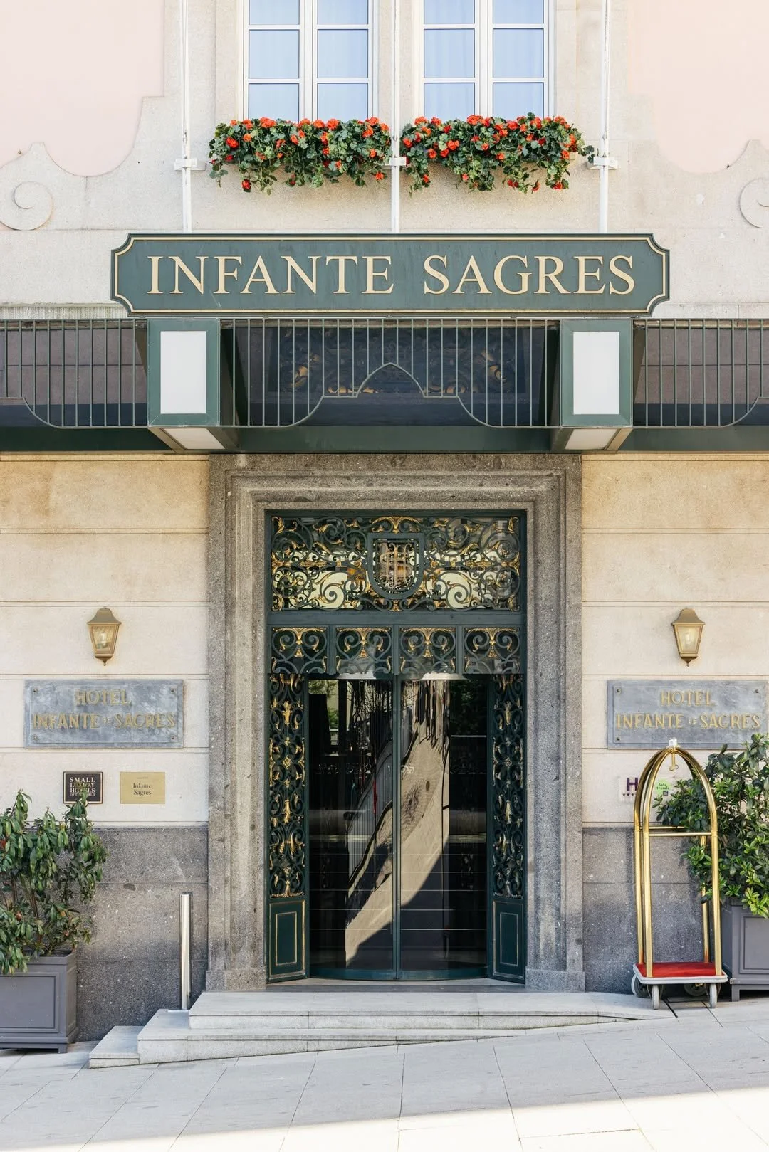 Front entrance of a hotel named 'Infante Sagres' with ornate iron gate, stone walls, and flower boxes above balcony