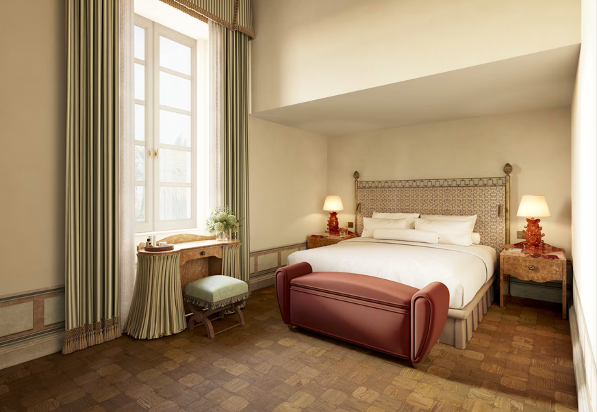 A hotel room with a large bed, two bedside lamps, a window with curtains, and a small dressing table with a stool.