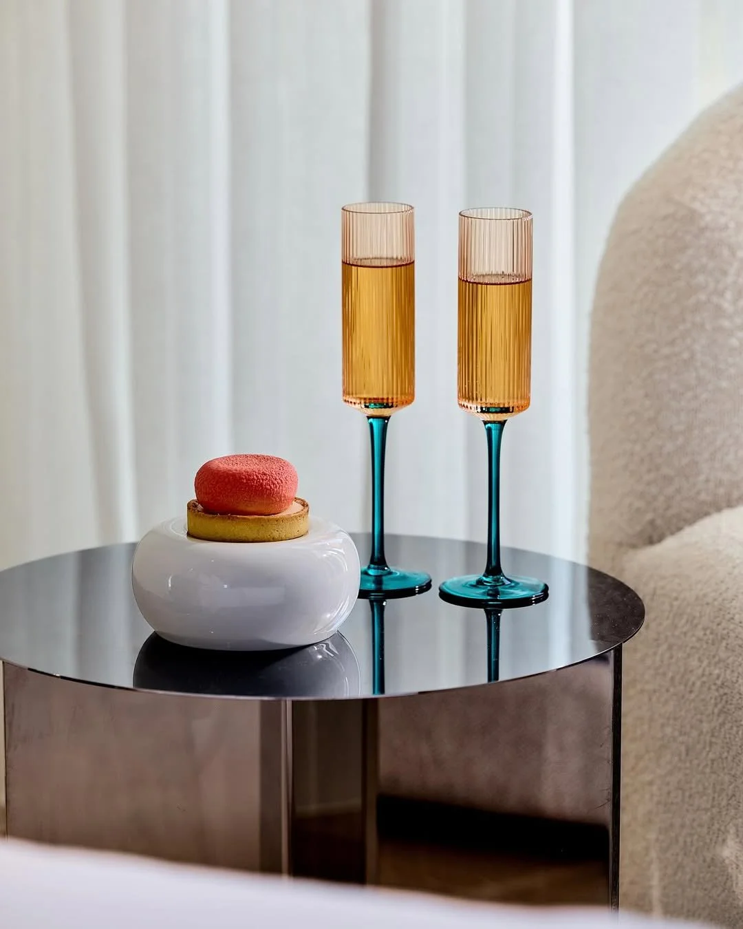 Two champagne glasses with pink liquid and a white vase with a pink macaron and cookie on a table.