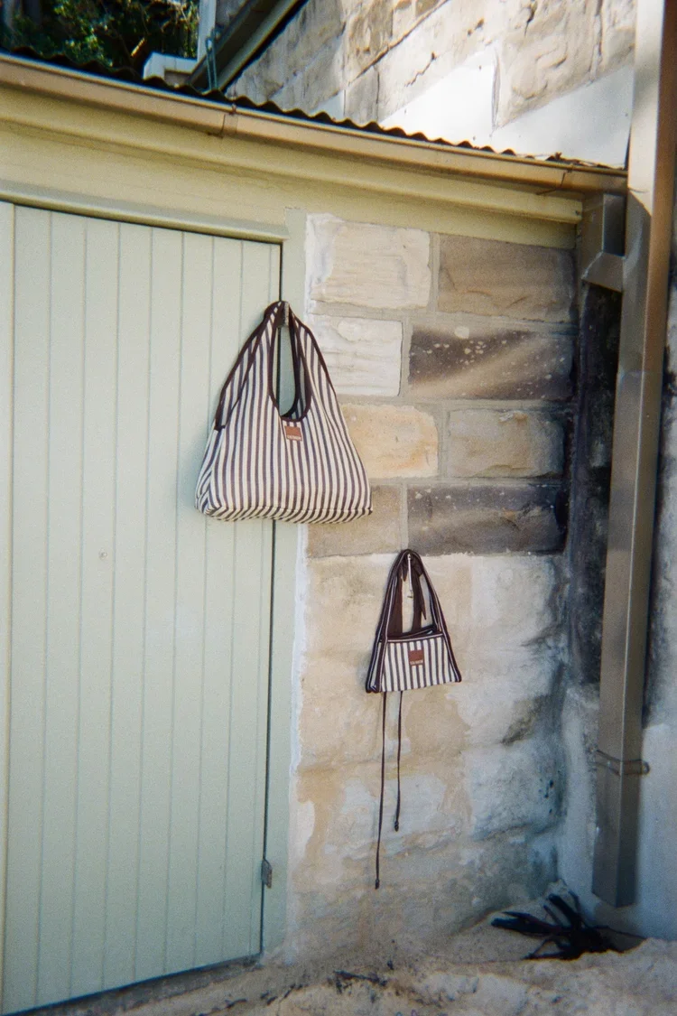Two striped bags hanging on a stone wall next to a light green door.