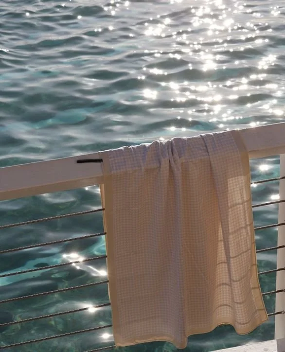 A beige towel hanging over a boat railing, with sparkling blue ocean water in the background.