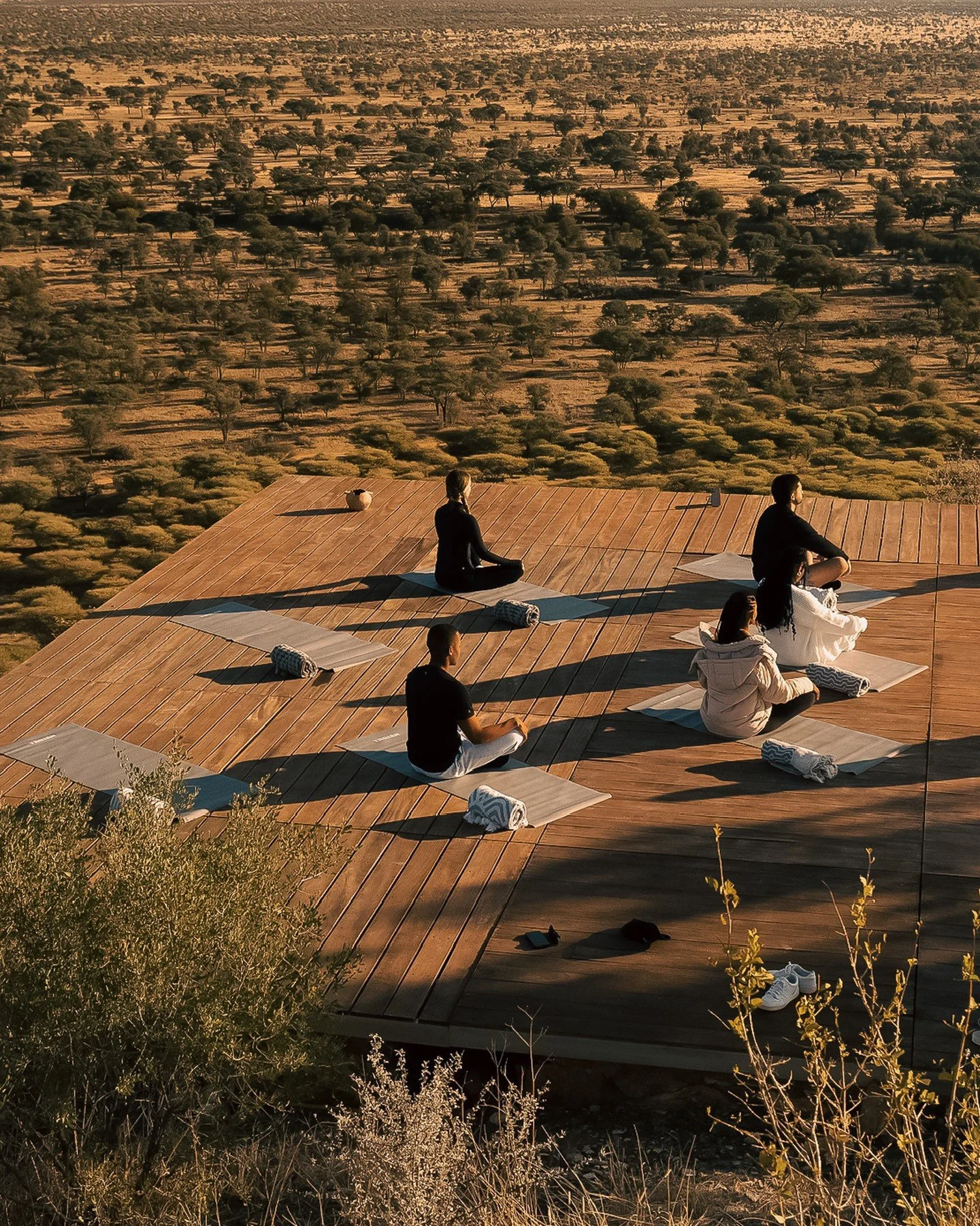 People practicing yoga on mats on a wooden deck in a desert landscape at sunset