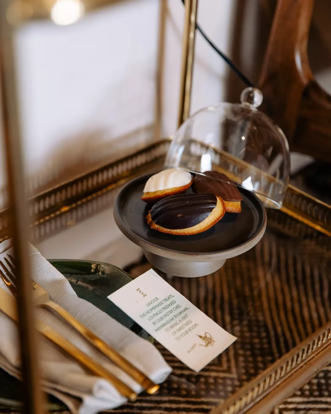 Assorted cookies on a black plate under a glass dome on a vintage wooden tray.
