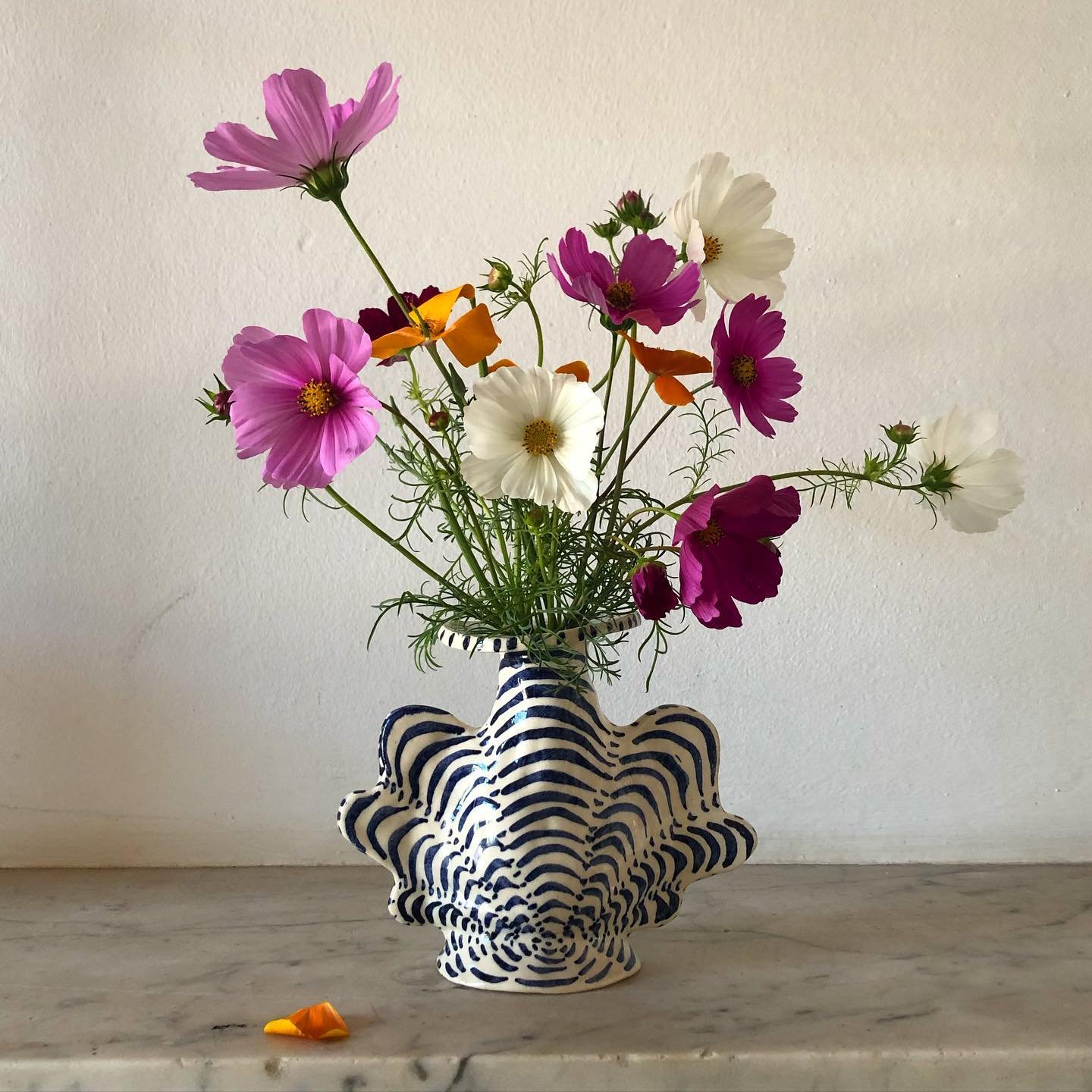 A bouquet of pink, white, and purple flowers in a black and white striped starfish-shaped vase on a marble surface against a plain white wall.