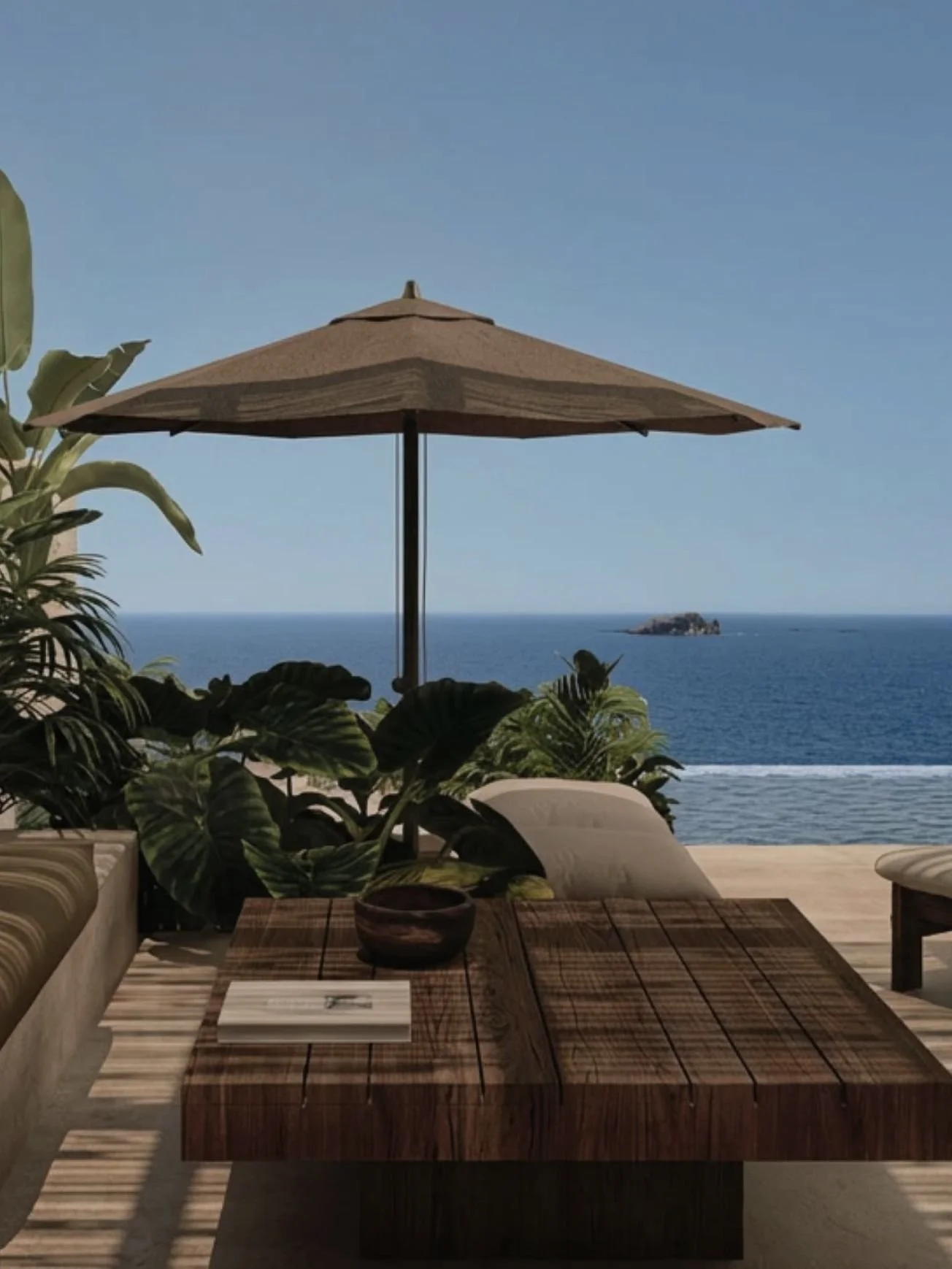 Outdoor patio with a wooden dining table, a large beige umbrella, green plants, and a view of the ocean and a small rocky island in the distance.
