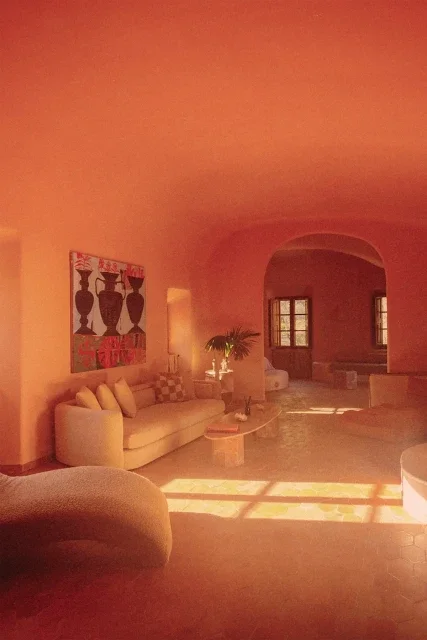 Living room with a cream-colored sofa, wall art, a potted plant, and sunlight streaming through windows.