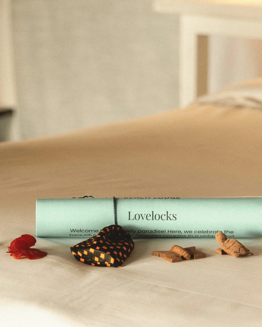 A rolled-up invitation or flyer labeled "Lovelocks" with small pieces of cork, a red flower, and a black and orange patterned cloth on a white surface.