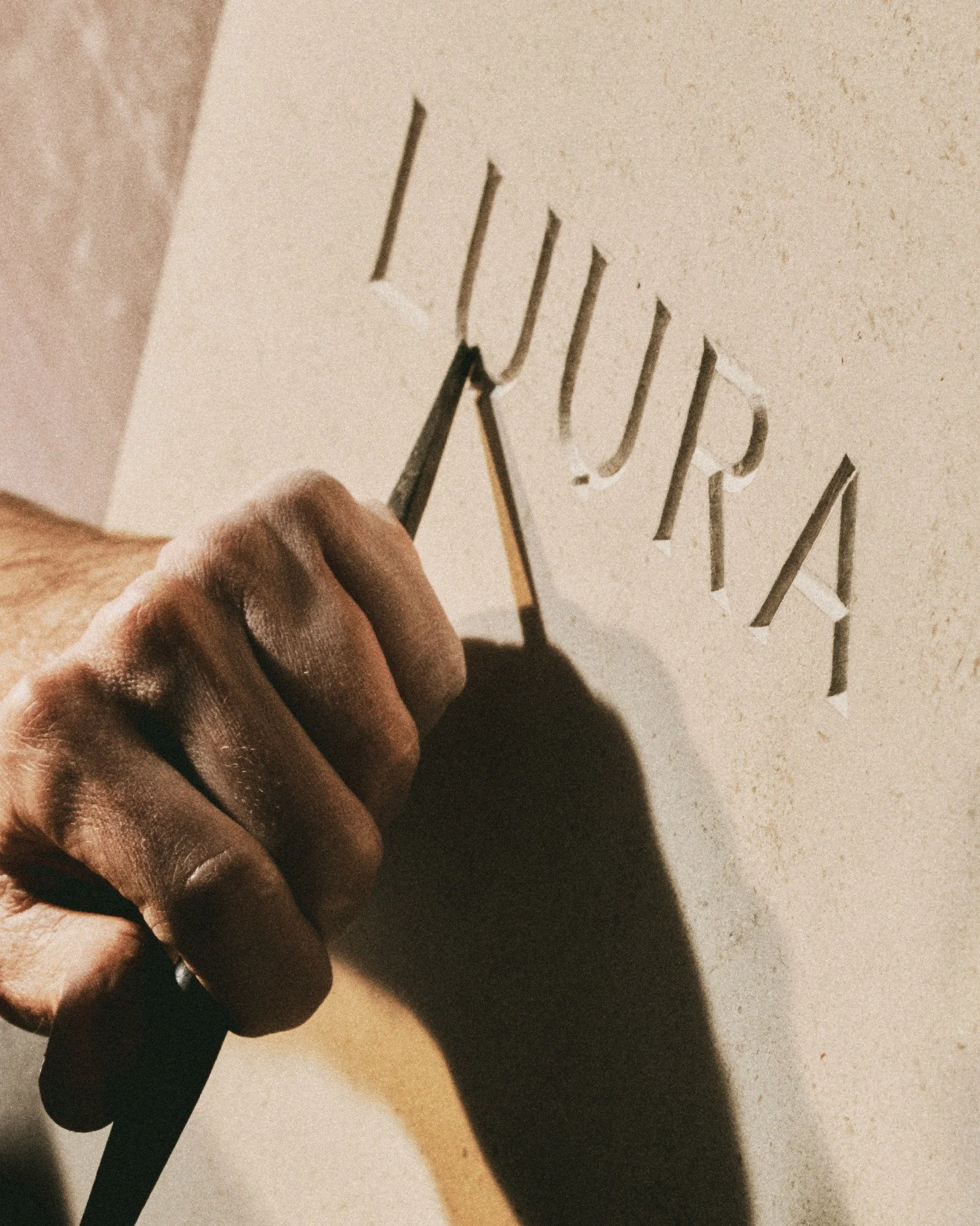 A hand with dark skin holding a paintbrush, painting black vertical lines on a white surface.