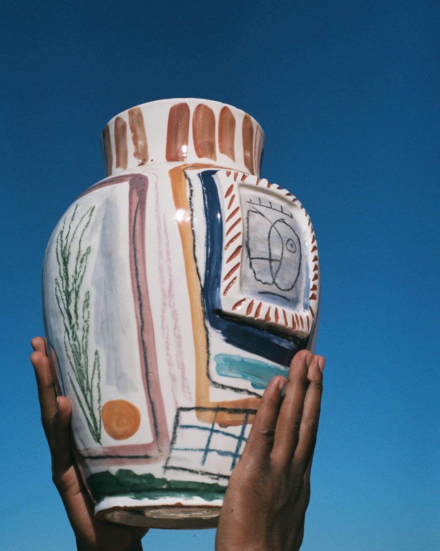 A person holding an abstract decorated vase with a blue sky background.