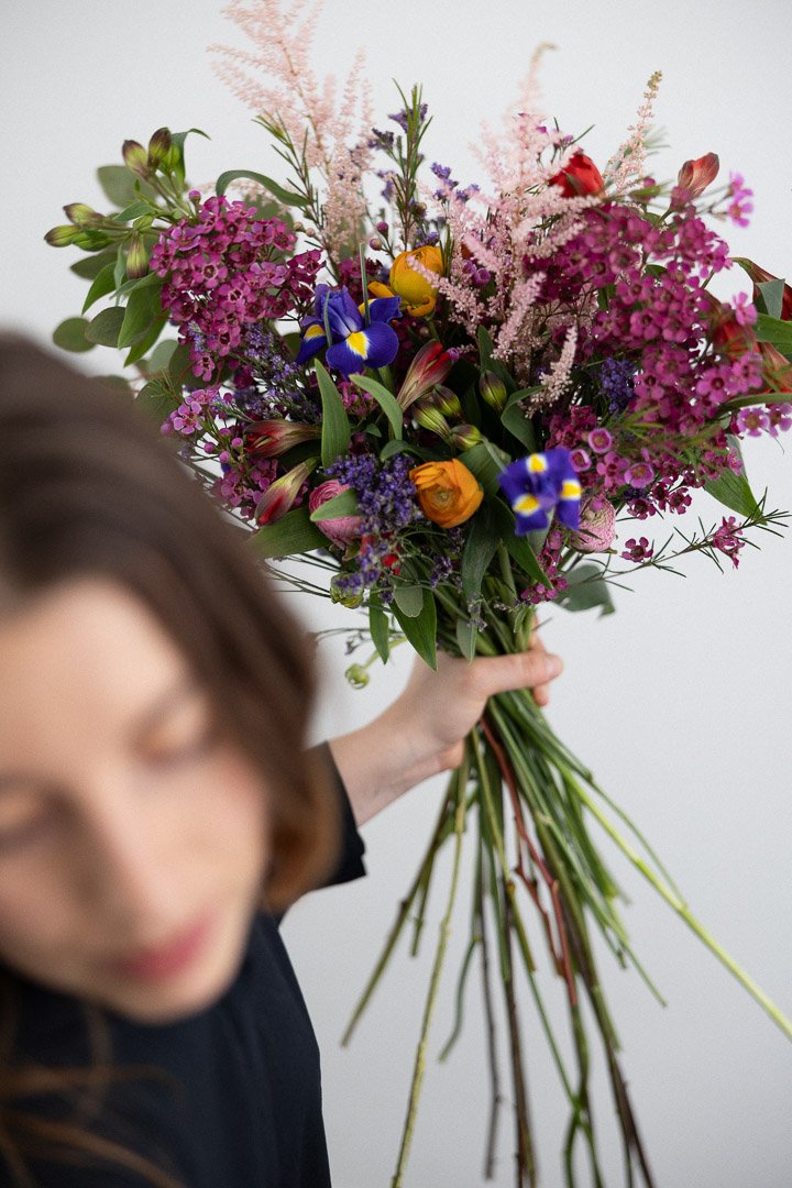 Une femme tient un grand bouquet de fleurs colorées, flou en premier plan.