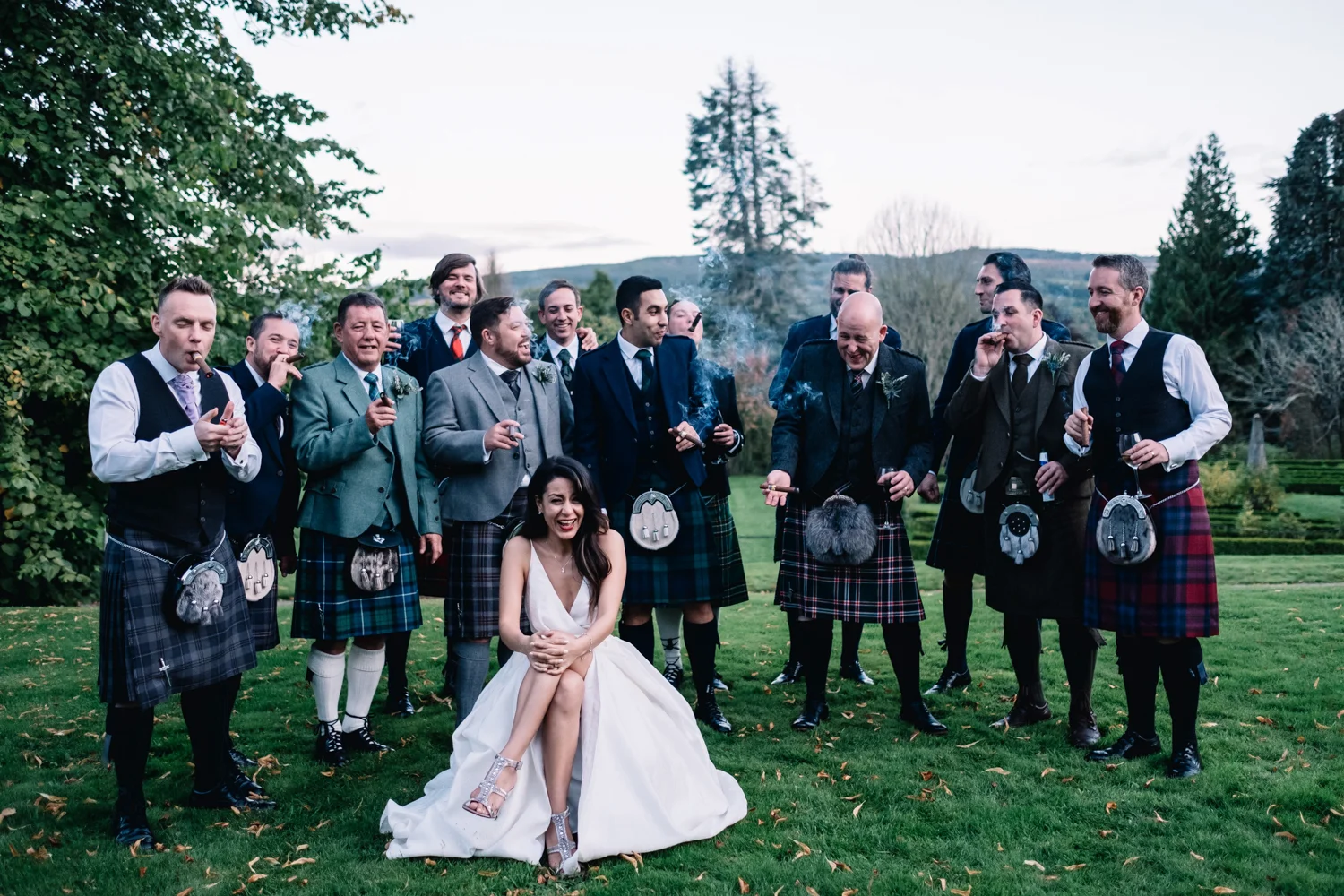  Bride sits and laughs - she is surrounded by the groom and the groomsmen who are smoking cigars. 