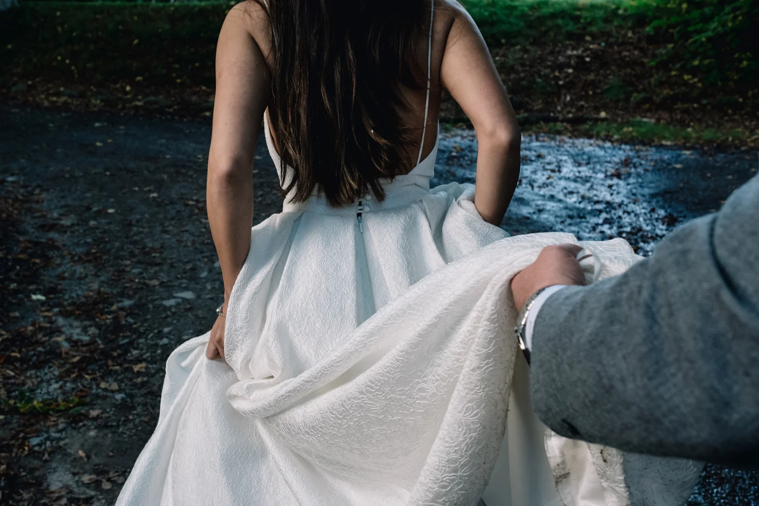  Groom holds bride's dress as they walk outside. 