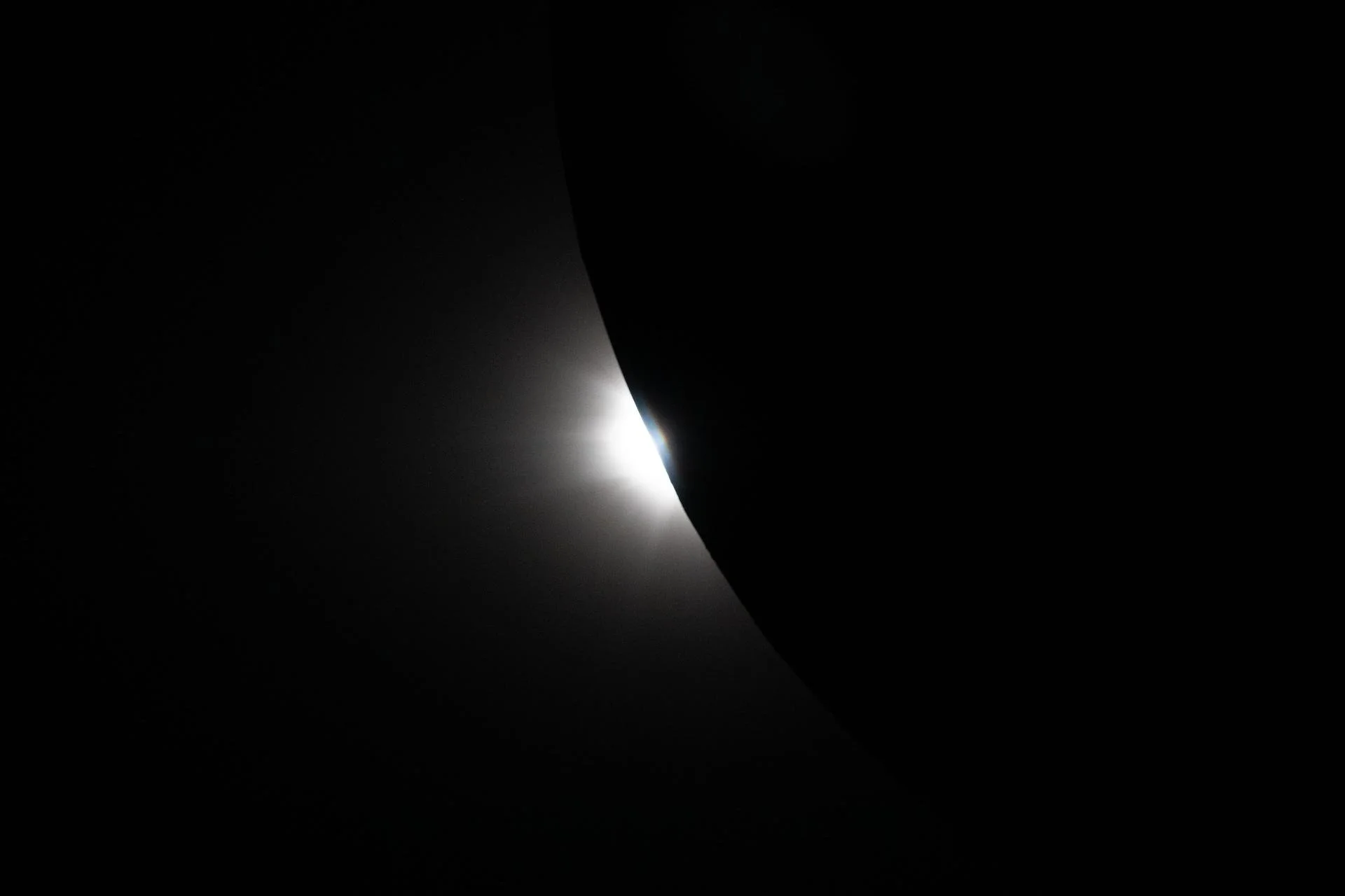 Partial solar eclipse with the moon covering part of the sun, creating a dark silhouette with a bright ring of sunlight, and a faint rainbow-like halo visible at the edge.
