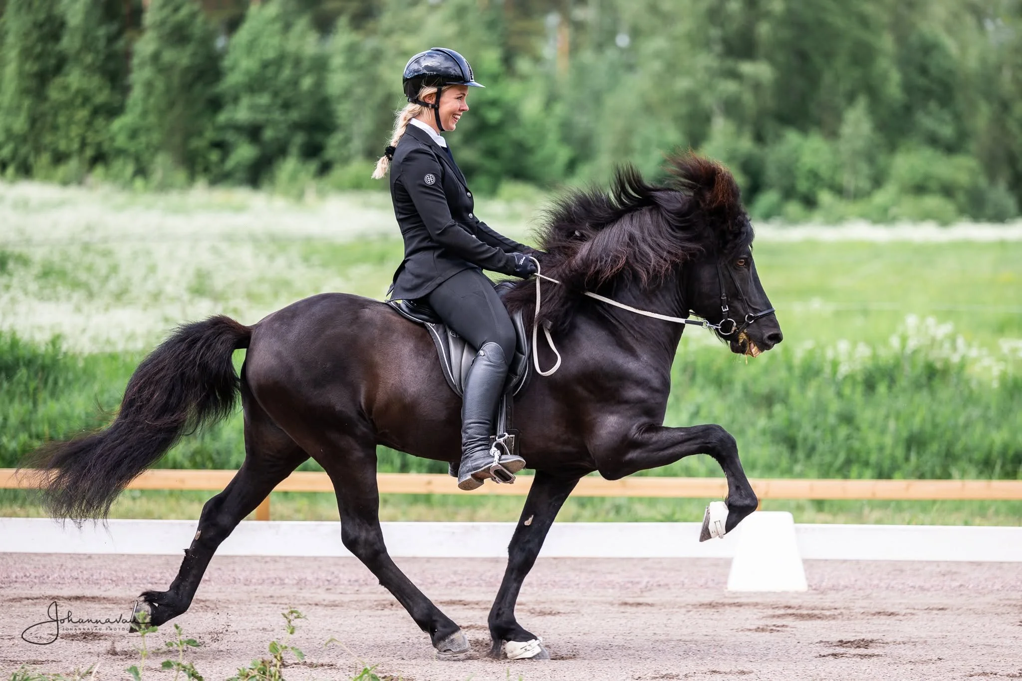 Nuori nainen ratsastelee mustalla hevosen ja kilpailuasuissaan green ympäristössä.