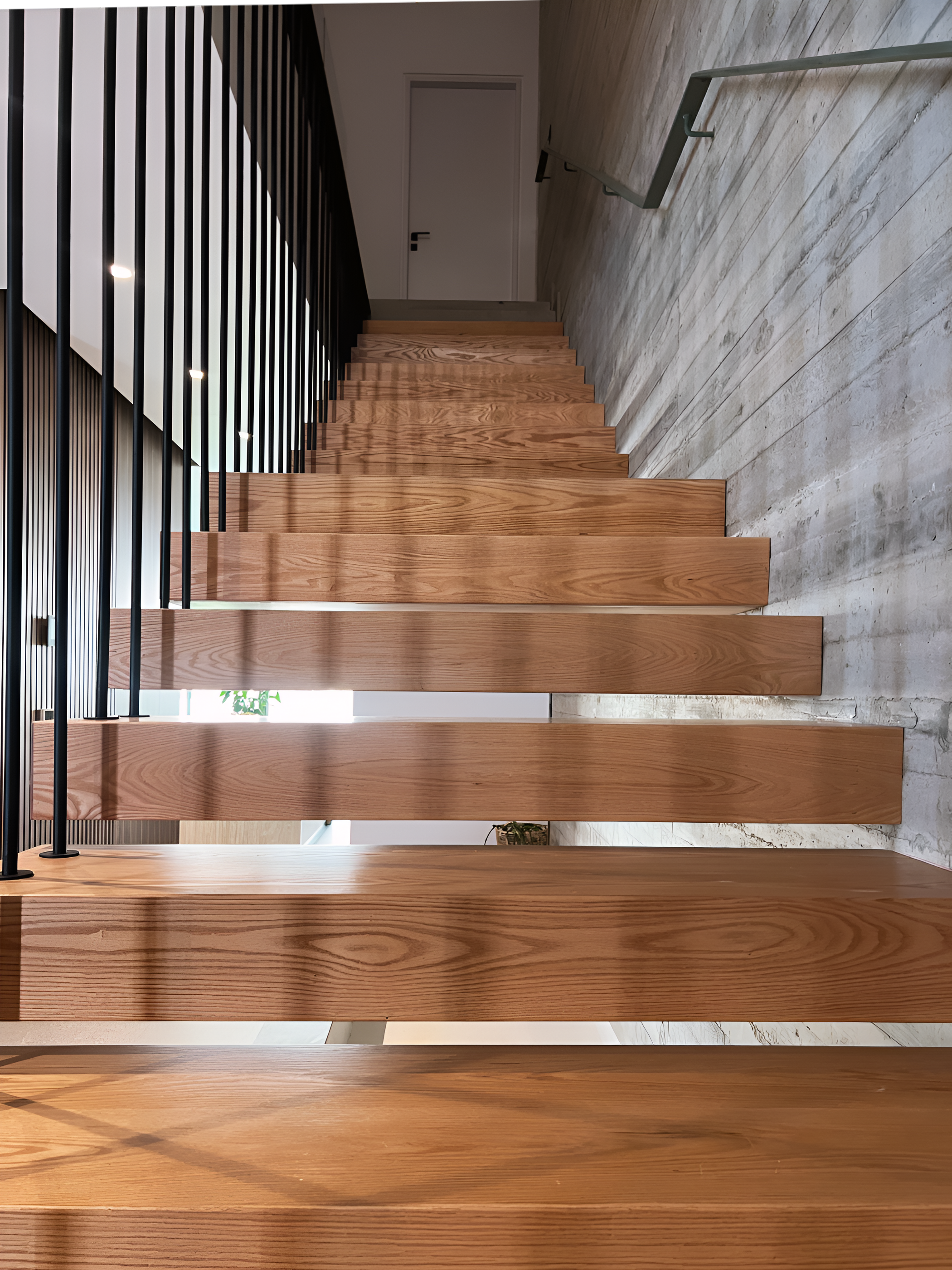 Wooden staircase with metal railing in a modern interior setting with a door at the top and a plant visible in the background.
