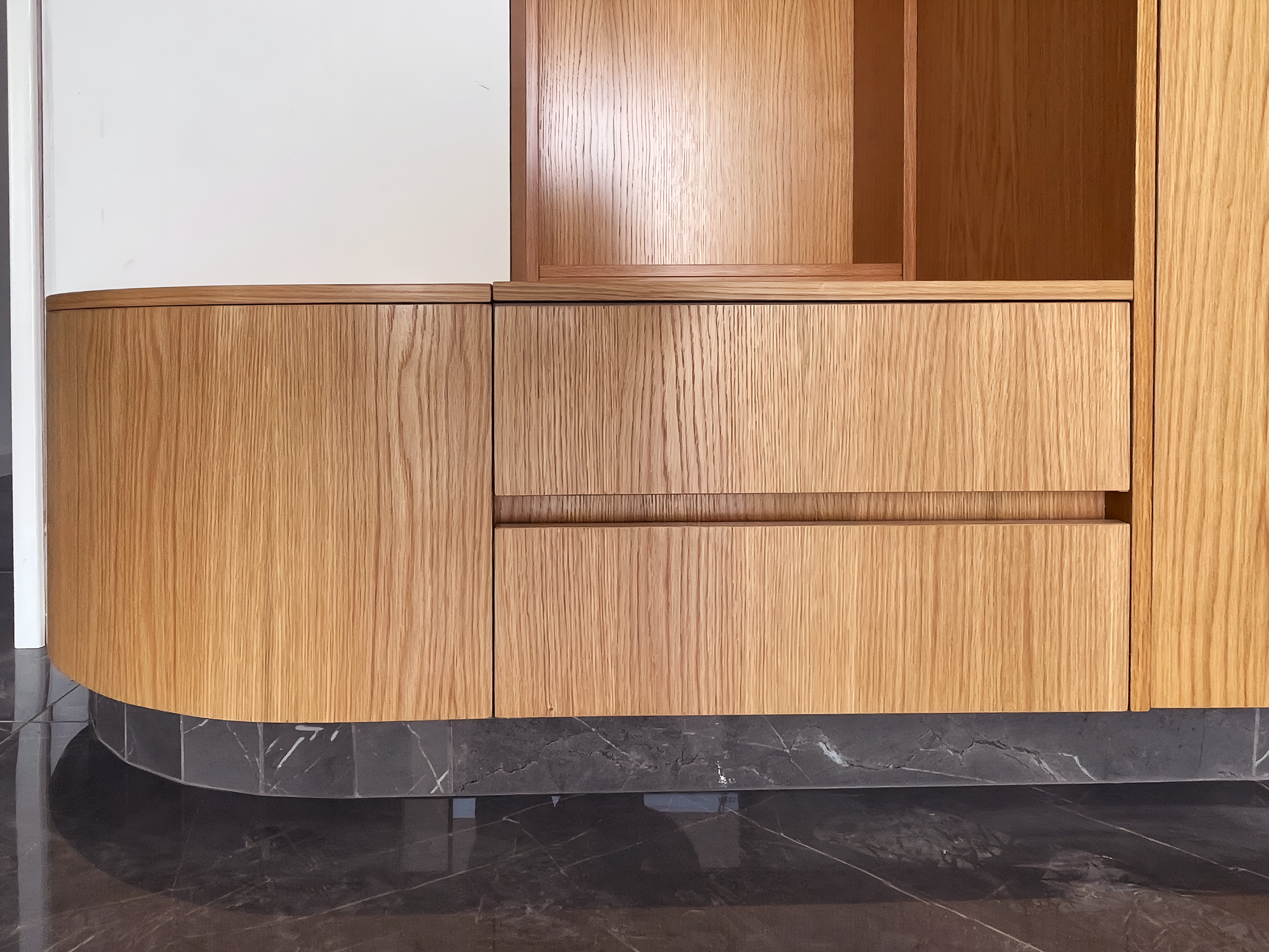 A curved wooden reception desk with a mix of light and dark wood finishes, located in a modern interior with marble flooring.