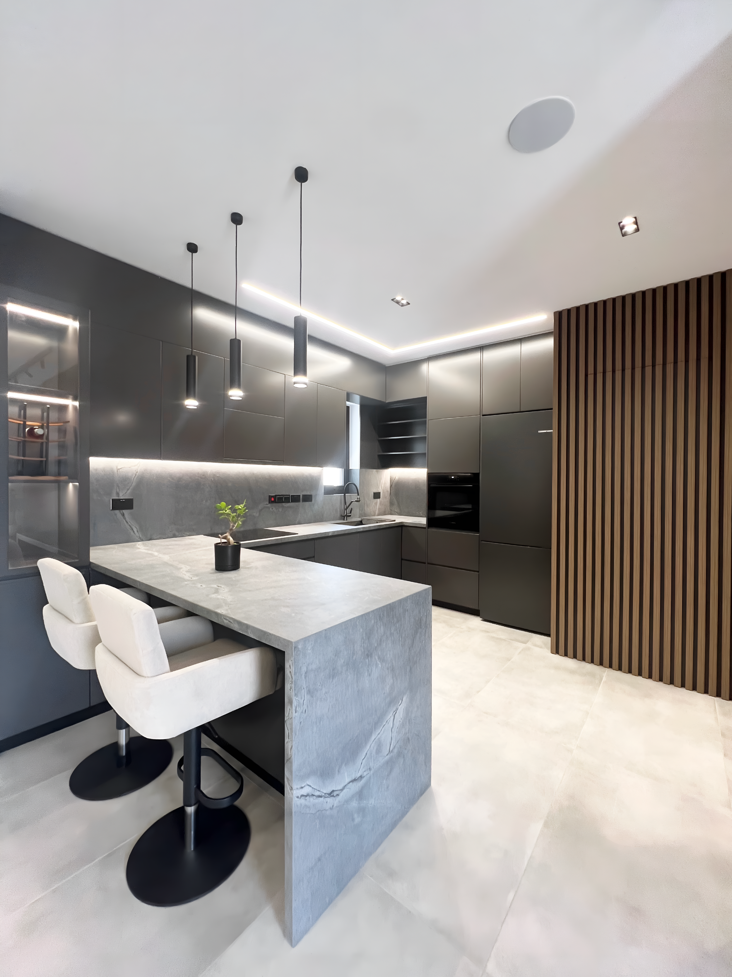 Modern kitchen with gray cabinetry, marble island with seating, black pendant lights, and wooden slat wall.