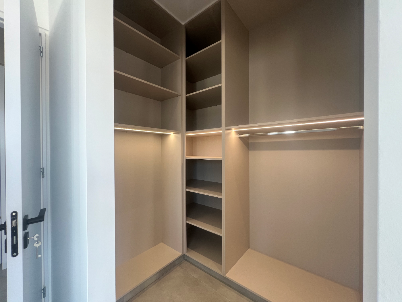 Empty built-in closet with multiple shelves and hanging rods, illuminated with integrated lighting.