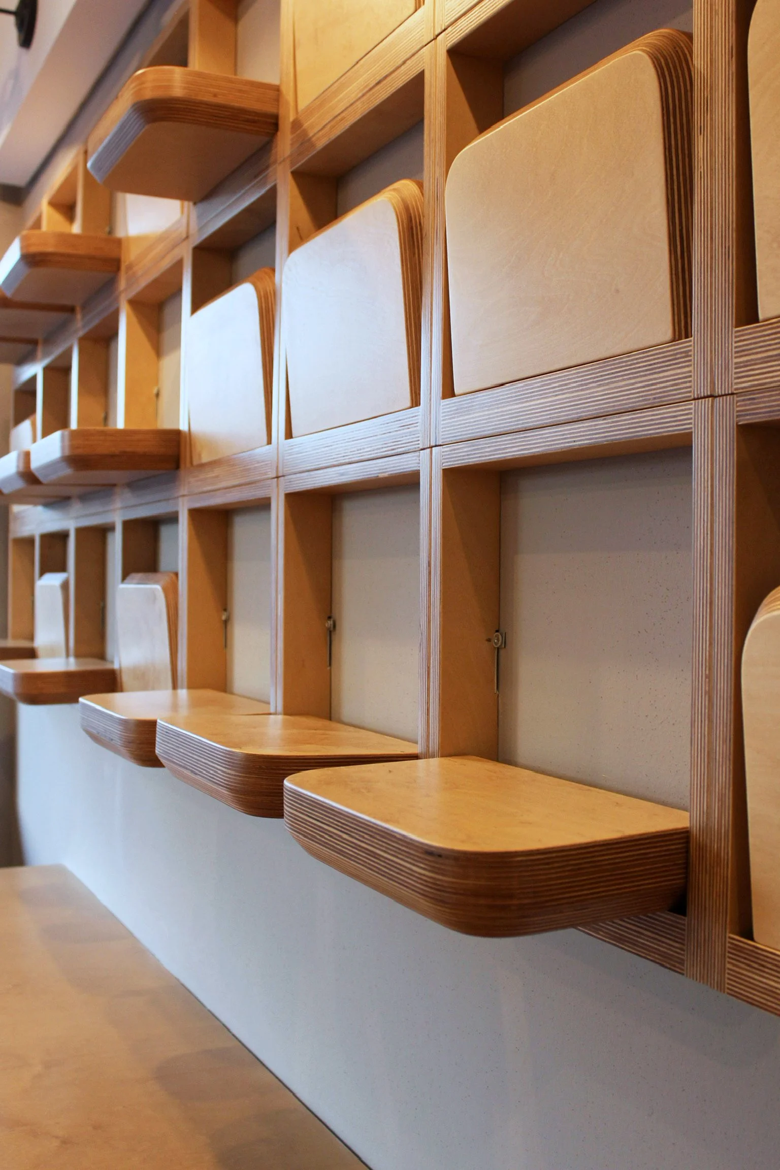Wooden wall-mounted desks with rounded edges attached to a wall in a staggered pattern.