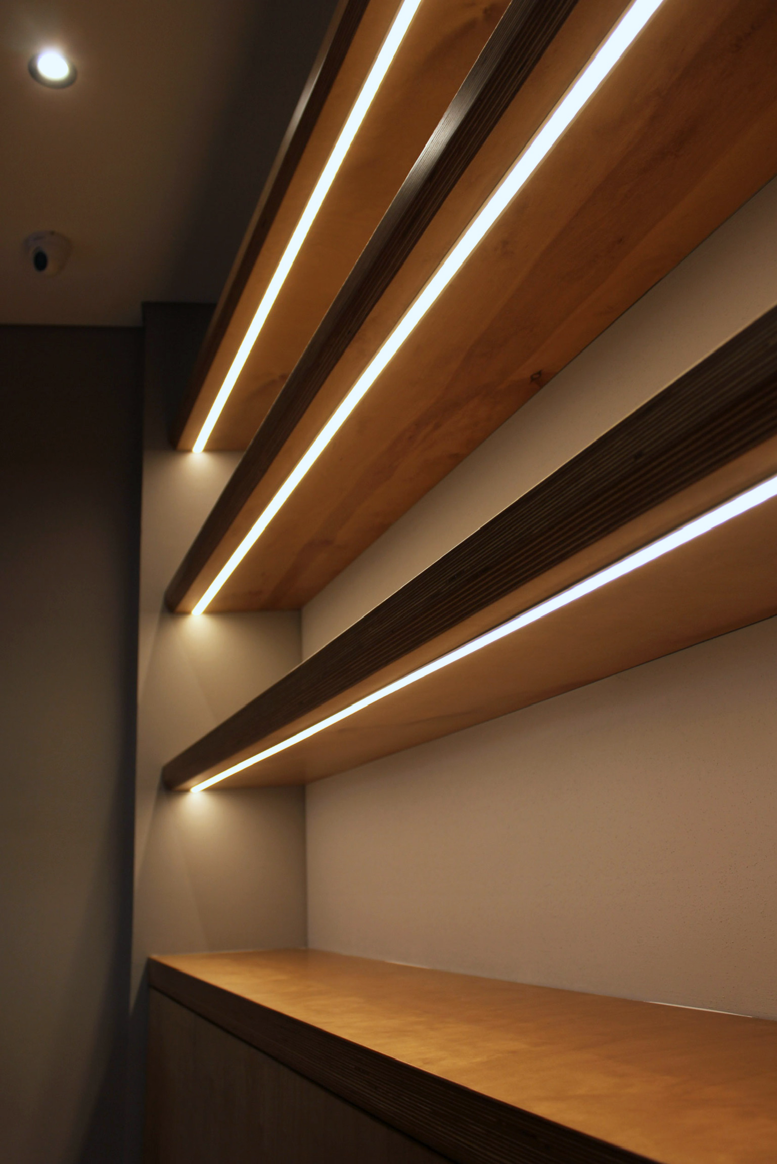 Interior wooden shelves with built-in lighting on a wall, viewed from below.