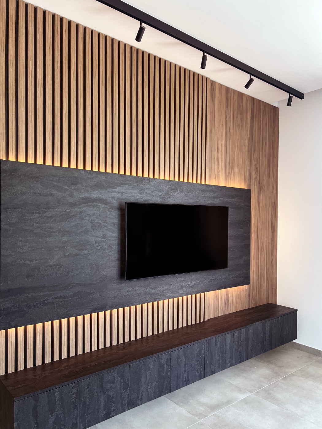Modern living room wall with a mounted flat-screen TV on a dark stone panel, wooden slat accent wall, and LED backlighting, with a dark wood media console below.