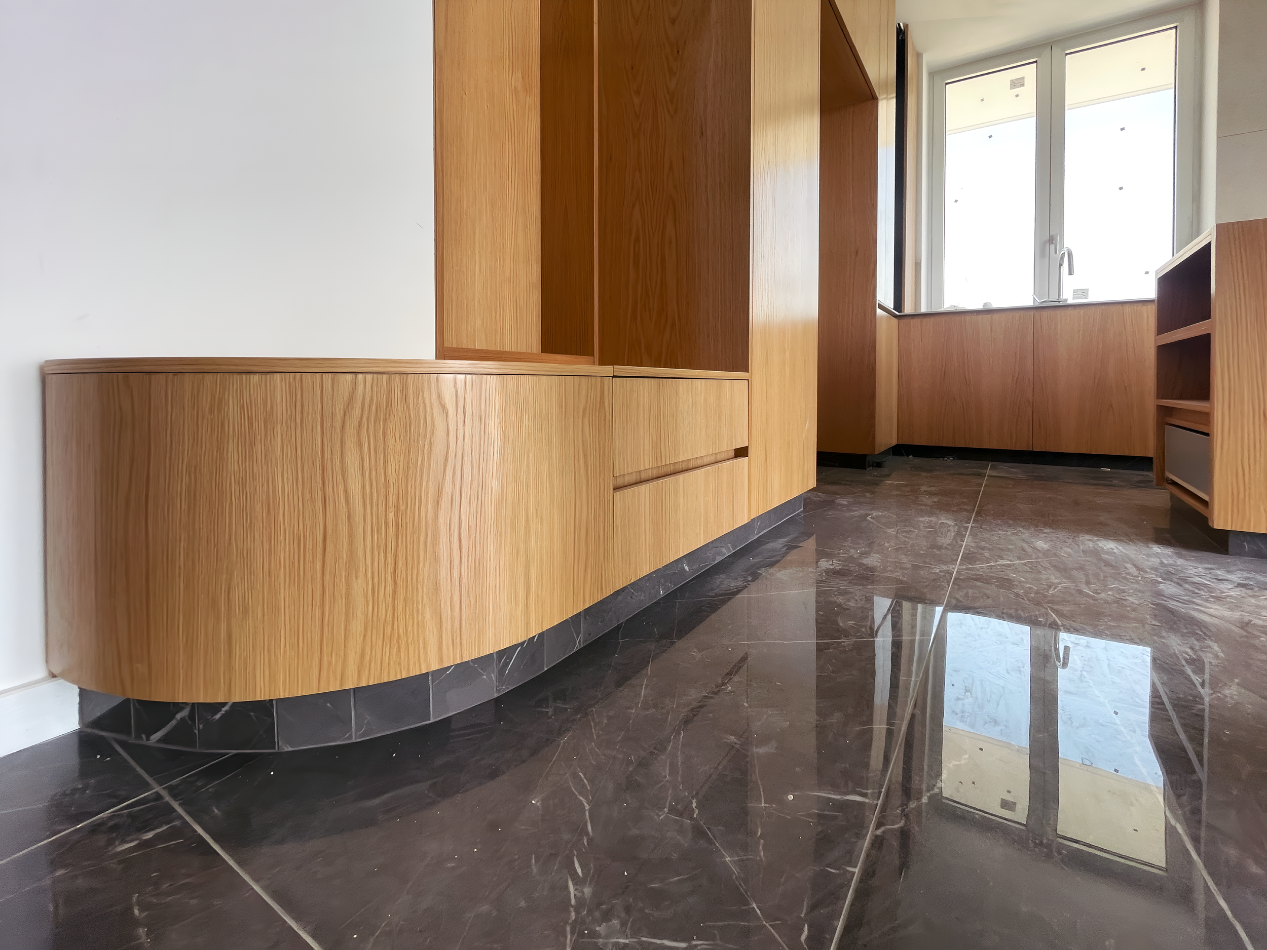 Modern kitchen with wooden cabinets and a window above the sink, dark marble tile flooring.