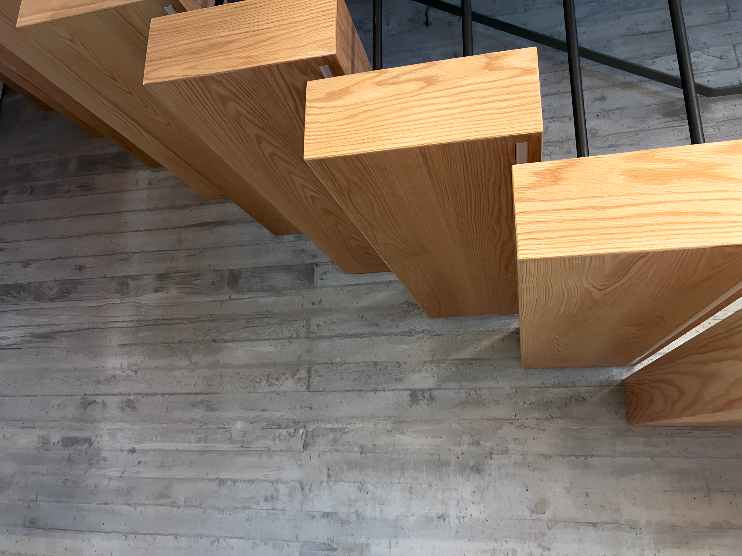 Close-up view of a staircase with wooden steps and black metal railings, with a wooden floor below.