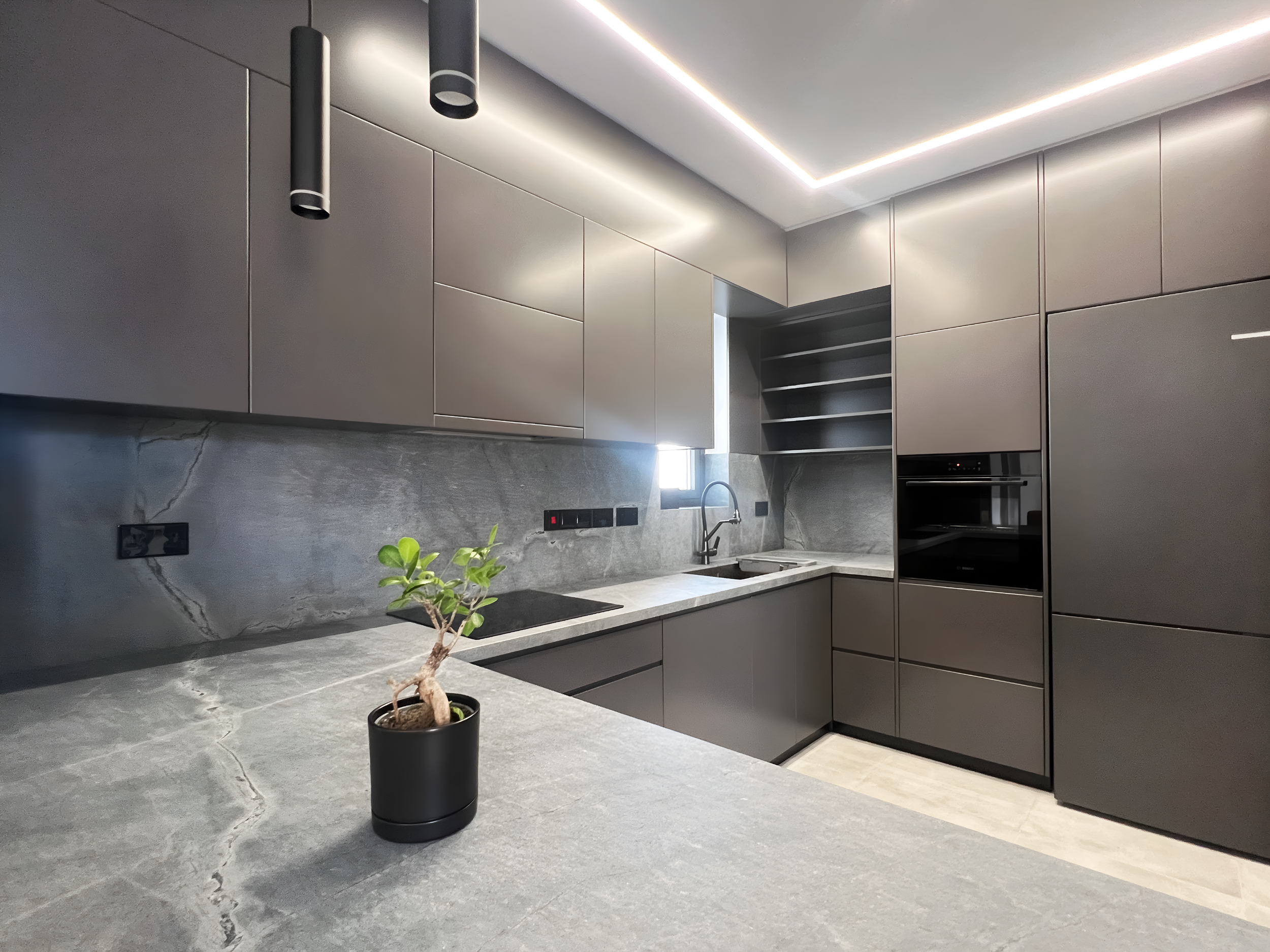 Modern kitchen with matte gray cabinets, a gray marble backsplash, a small potted plant, and recessed lighting in the ceiling.