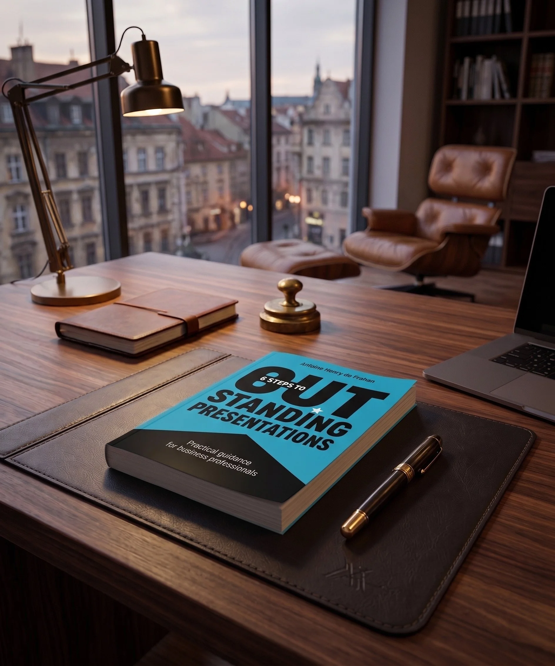 A wooden desk with a black leather desk mat, gold and black pen, a book titled "6 Steps to Quite Standing Presentations" by Antoine Henry de Frahan, a closed wallet, and a gold and black desk lamp. In the background, a window with a view of city buildings and a partly cloudy sky.