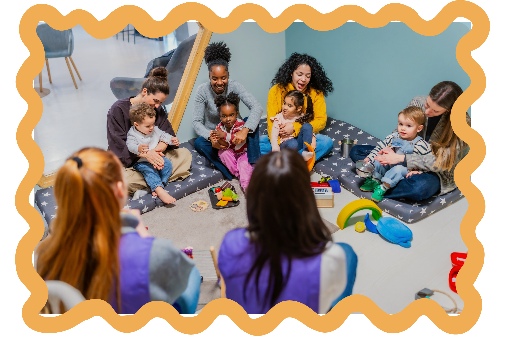 Group of moms and babies and toddlers sitting on a padded floor in a circle, engaging in play and conversation. Toys and play items are scattered around for group classes at Strong Roots OT in south NJ and Philadelphia.
