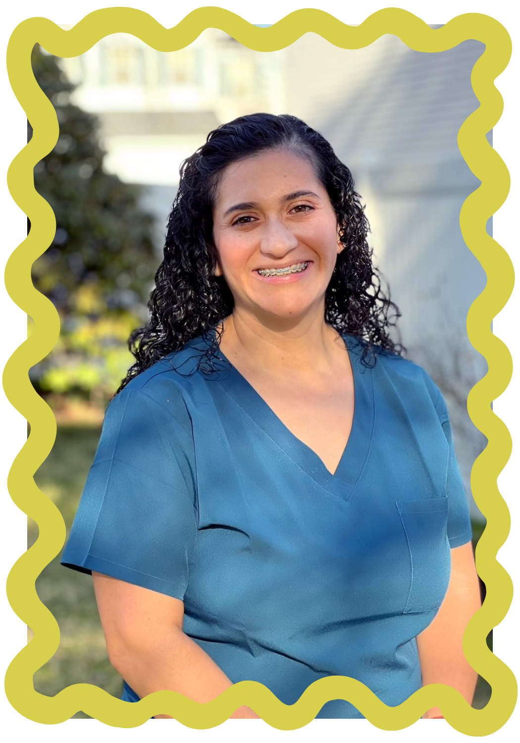 A photo of Paula Bradley, the owner of Strong Roots OT and occupational therapist specializing in maternal health and pediatrics. She has curly dark hair, is wearing braces, and is smiling in front of a blurred outdoor background. Green frame.