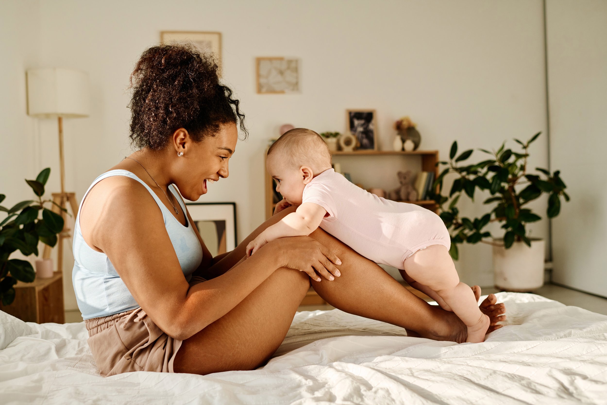 A woman and a baby playing and laughing on a bed  for Strong Roots OT in Philadelphia and South NJ.