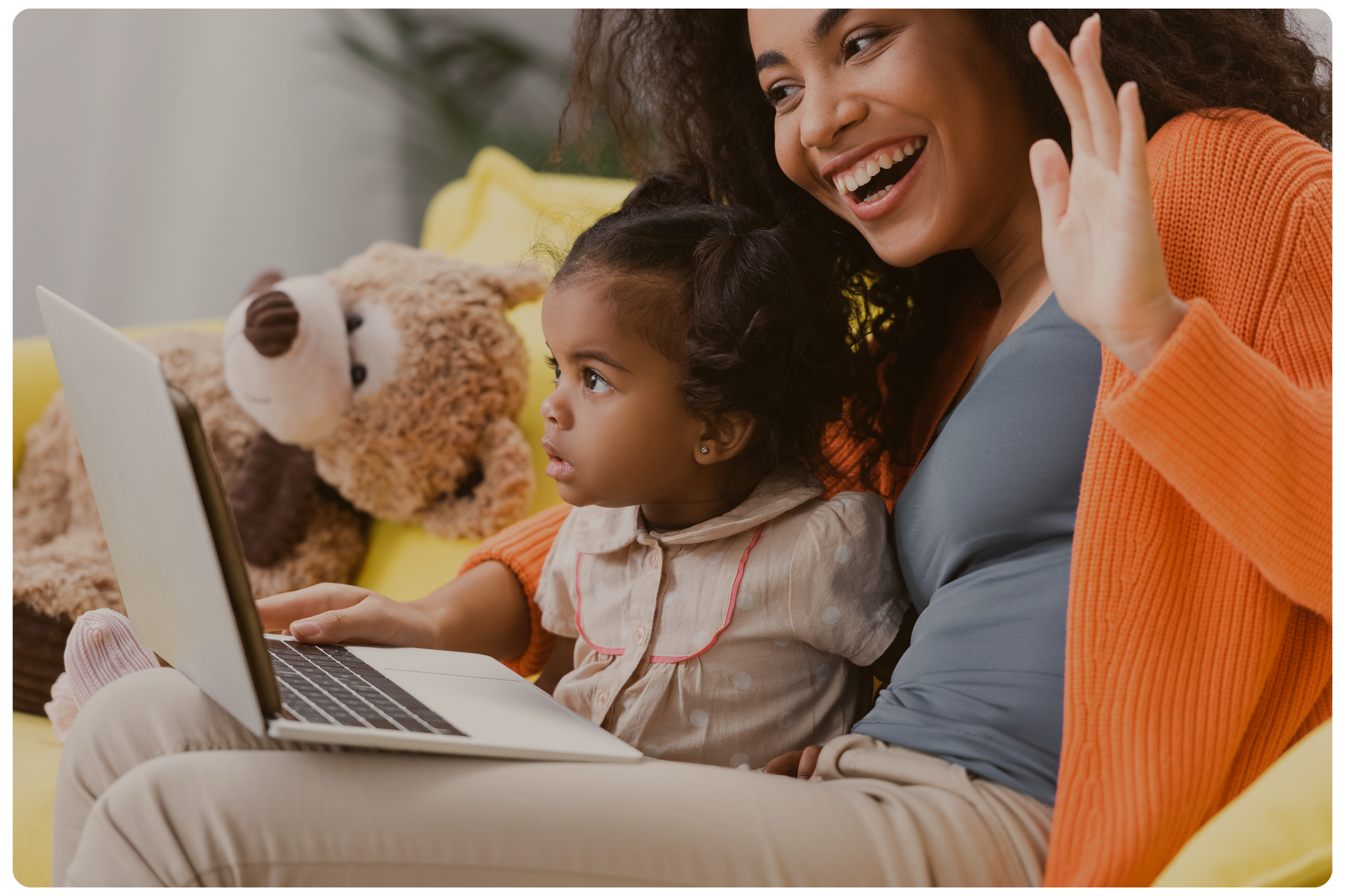 A woman with curly hair and a girl sitting on a couch using a laptop computer, with a teddy bear in the background to represent Strong Roots OT, an occupational therapy clinic in south New Jersey & Philadelphia that specializes in maternal health.