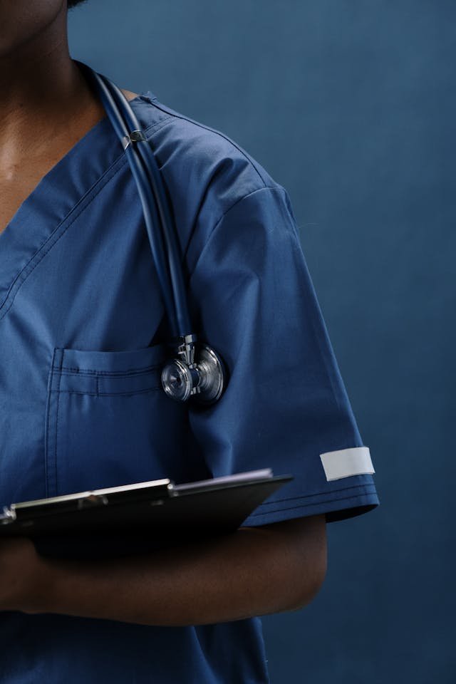 Healthcare professional in blue scrubs holds a clipboard with a stethoscope around their neck, illustrating healthcare professional coaching and leadership development for clinicians navigating career growth and organizational responsibilities.