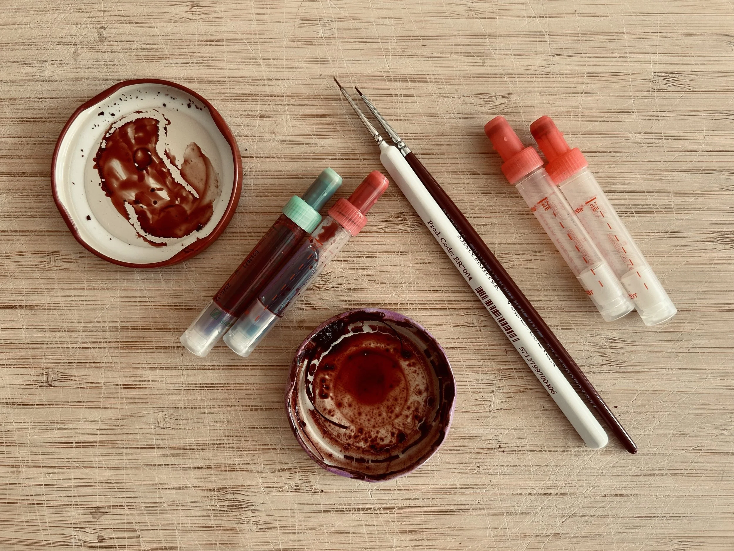 Blood samples in test tubes, a pipette, and a small dish with blood on a wooden surface.