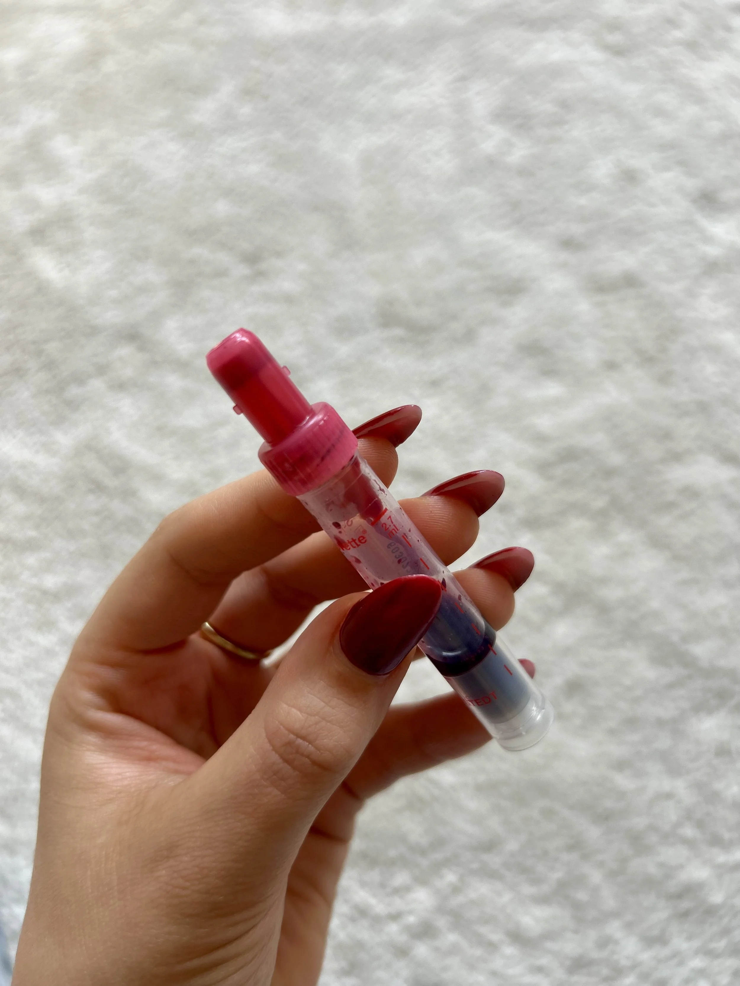 Person holding a syringe filled with red liquid against a light textured background.