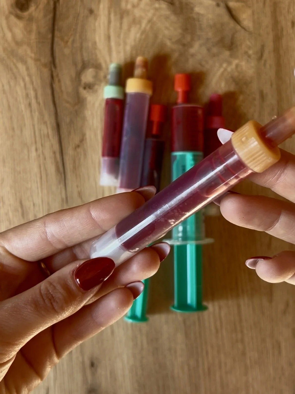 Close-up of a hand holding a small tube filled with blood, with other similar tubes in the background on a wooden surface.