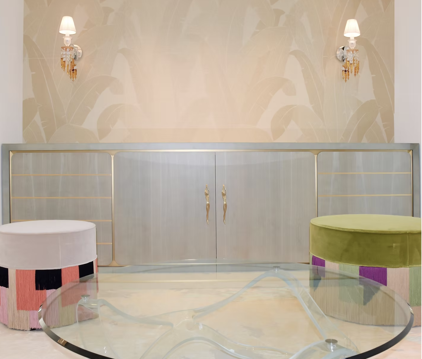 Intérieur de salon avec deux lampes murales, un meuble en bois clair avec portes métalliques et deux sièges rond en tissu, un jaune et l'autre rose, autour d'une table en verre.