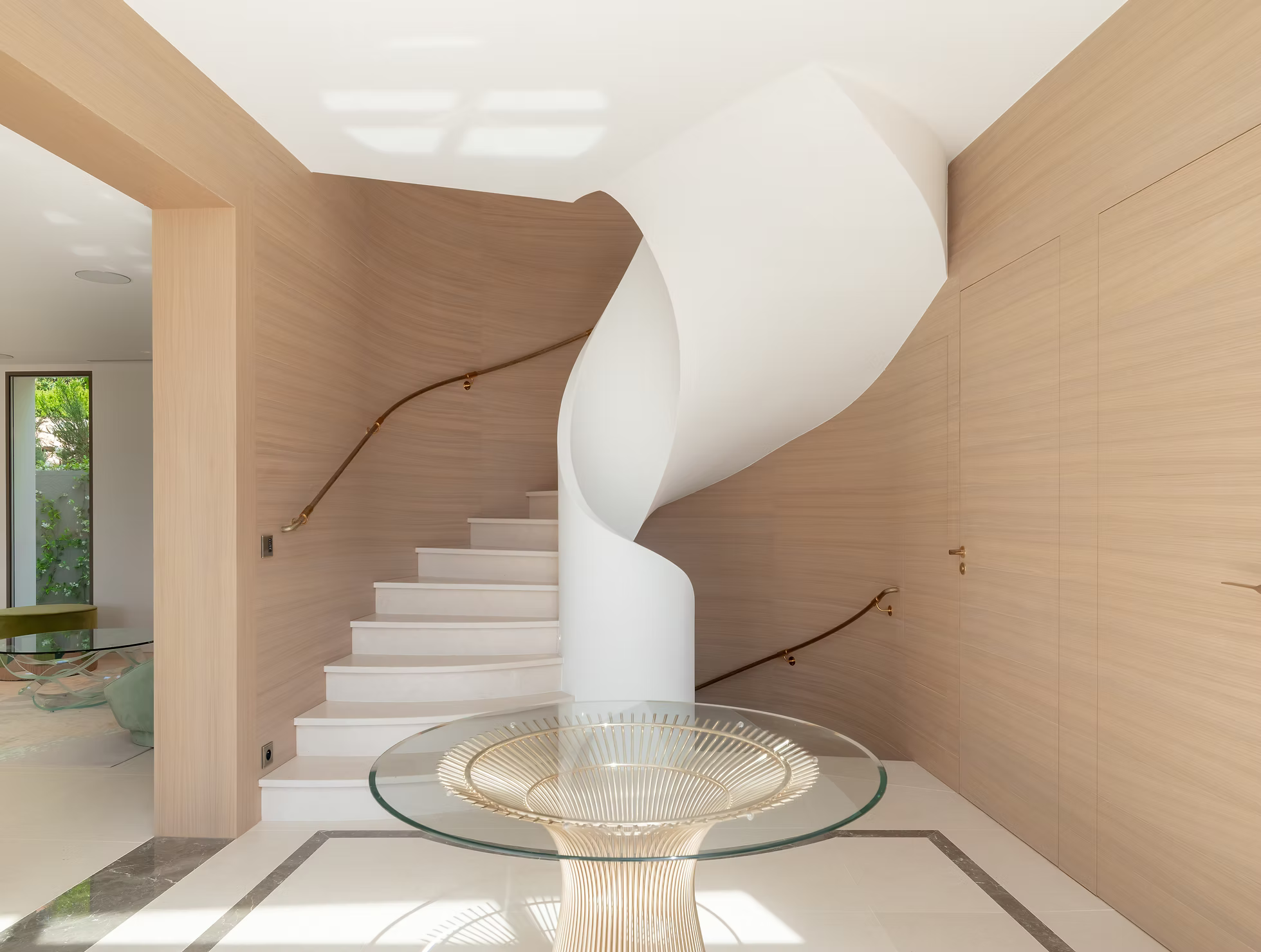 Un escalier en colimaçon blanc avec une rampe en bois dans un intérieur moderne avec des murs en bois clair et un plafond blanc courbe, une table en verre avec un éclairage design en dessous