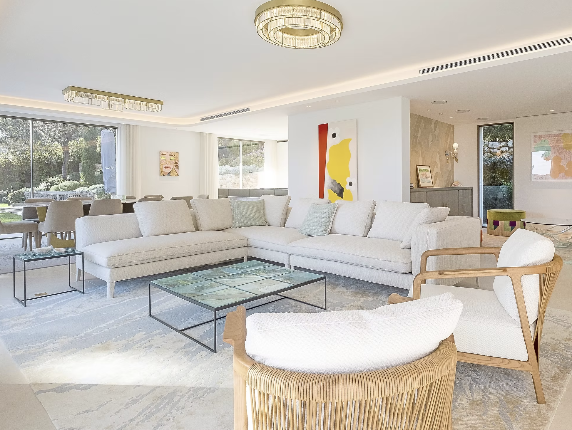 Salon moderne avec canapés blancs, tables en verre, œuvres d'art sur les murs, grandes fenêtres laissant entrer la lumière naturelle, et décor élégant.