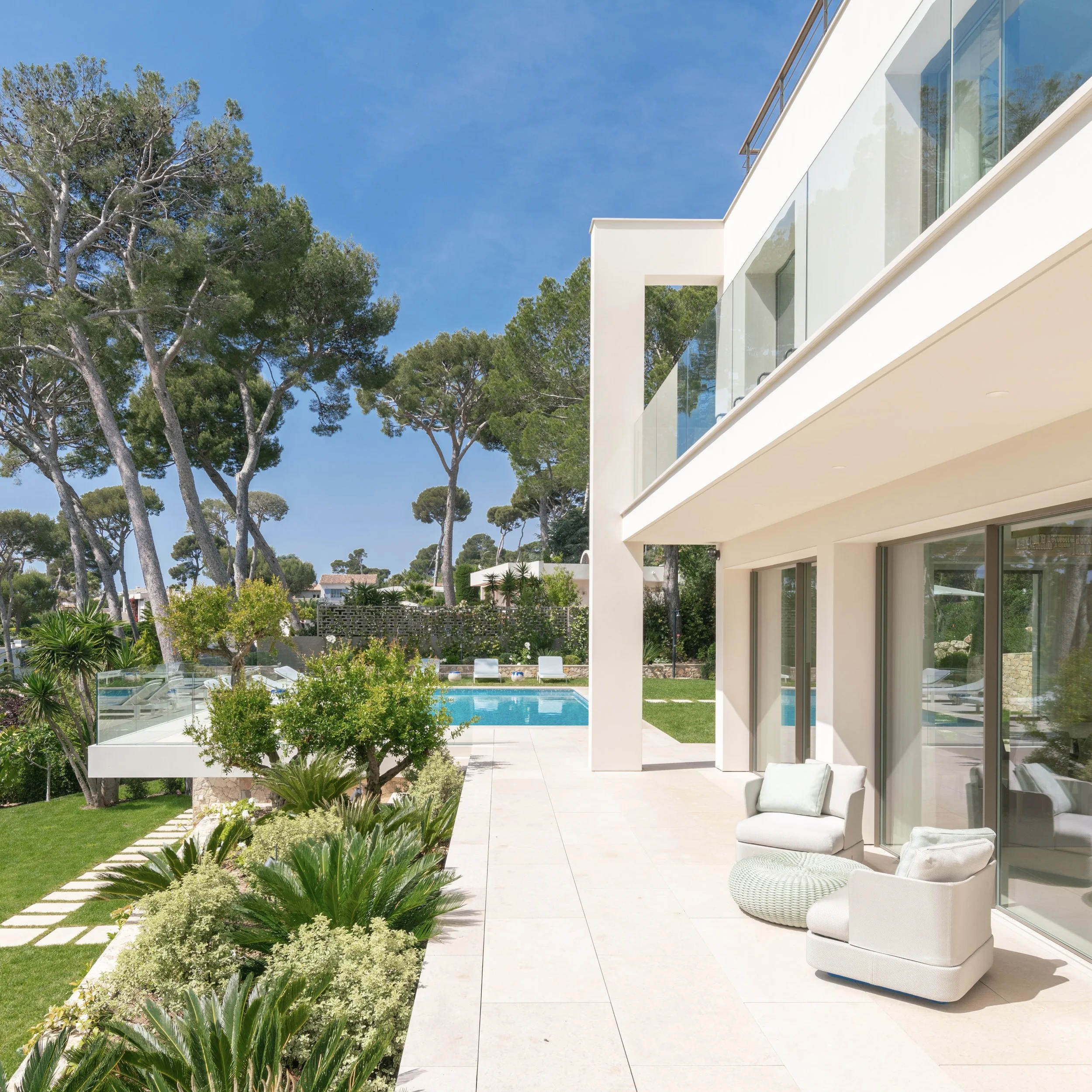 Balcon de maison moderne avec vue sur jardin et piscine, fauteuils blancs et plantes vertes