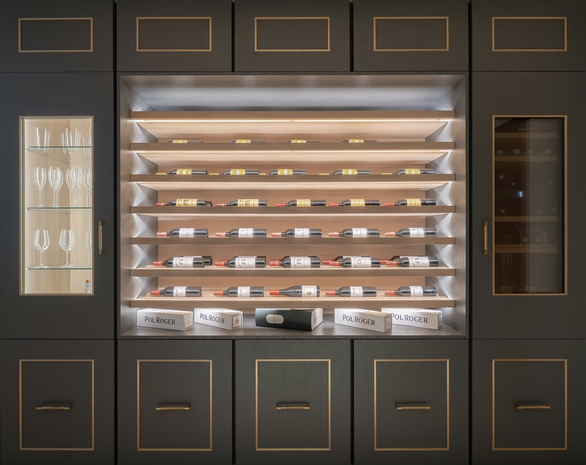 Une cave à vin moderne avec des étagères en bois éclairées, contenant des bouteilles de vin allongées, et un mur en ardoise foncée avec des armoires de rangement.